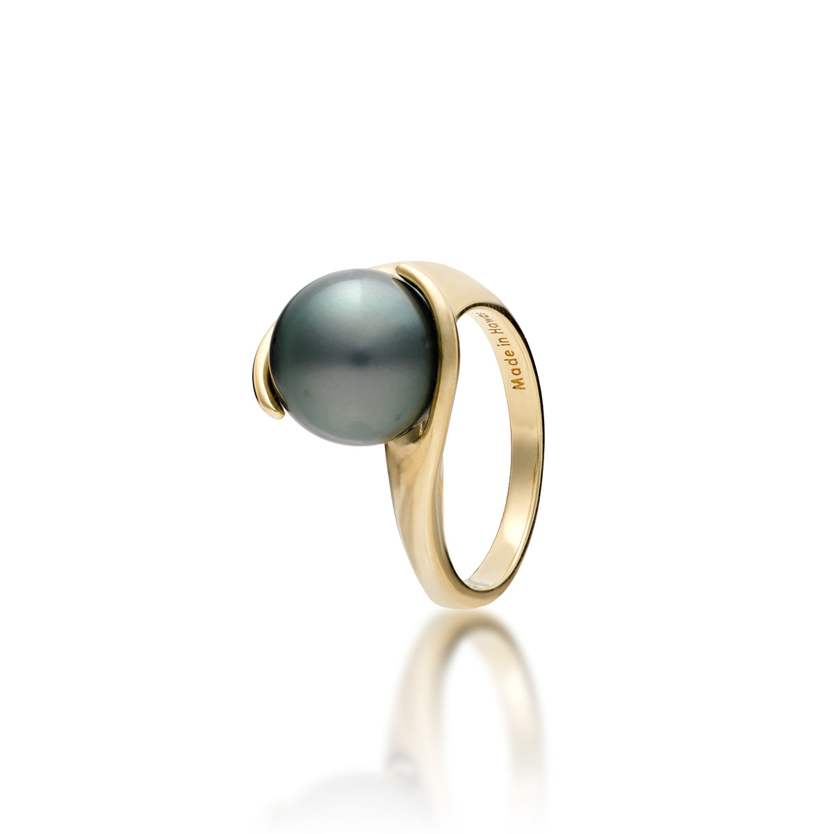 A simple 14k yellow gold ring featuring a Tahitian black pearl with curved gold wrapped around each side, shown on a clean white background with a soft reflection below. The inside of the band is engraved with 'Made in Hawaii'.