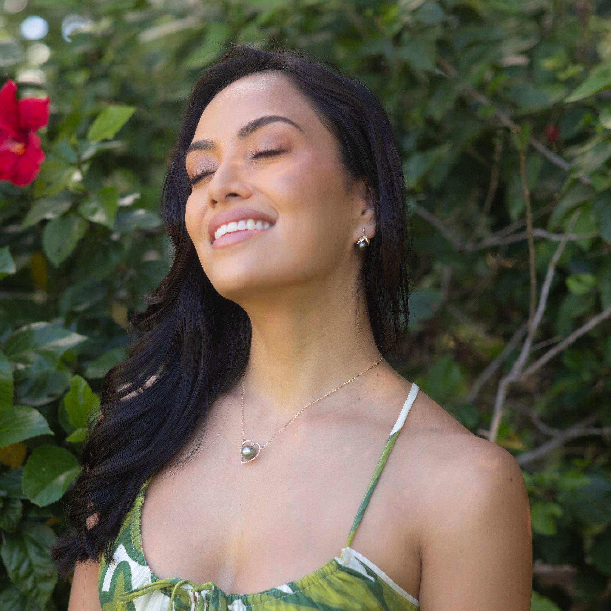 Smiling Woman wearing heart necklace and Maile Tahitian Black Pearl Earrings in Gold