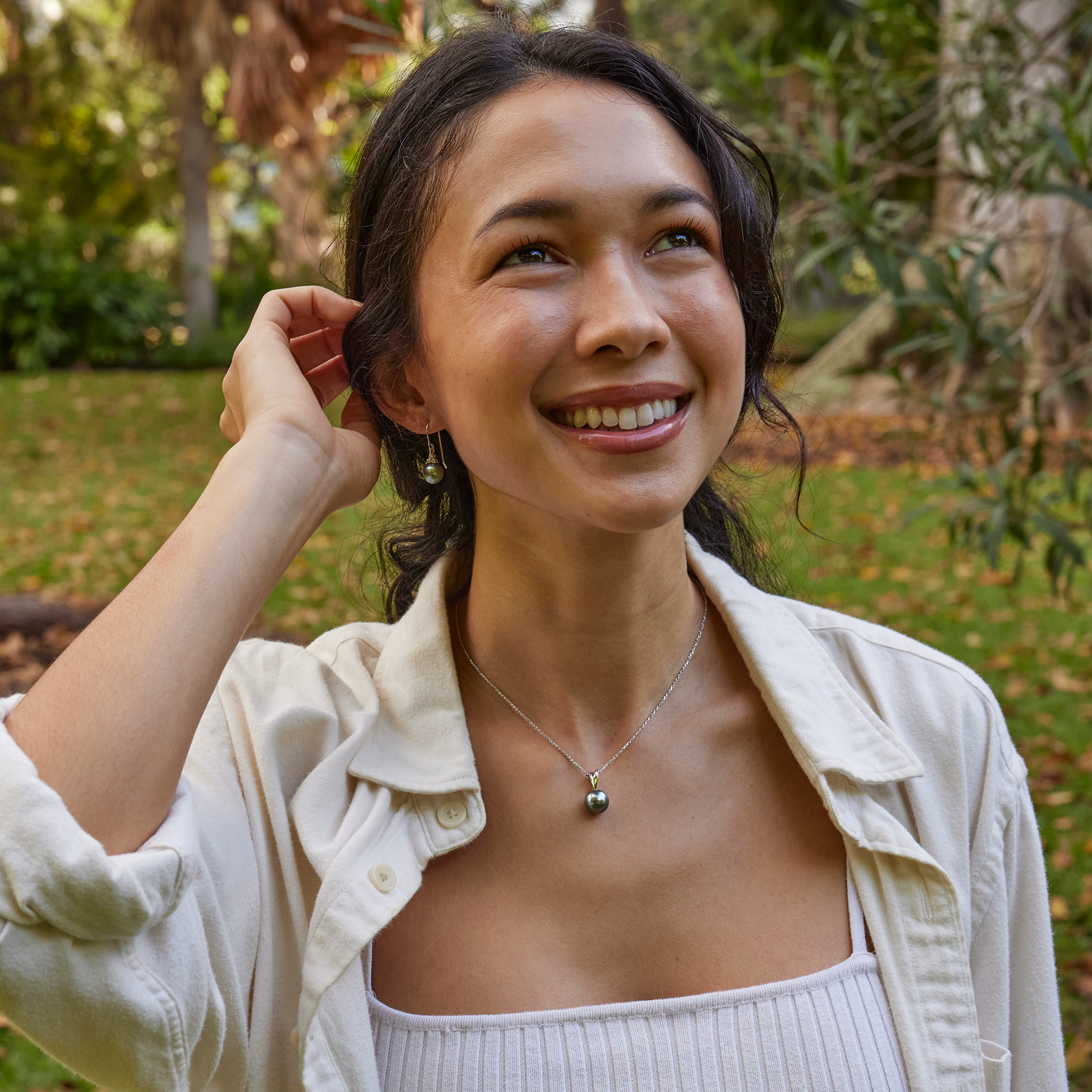 Tahitian black pearl earrings and matching necklace worn by a smiling woman in a white shirt.