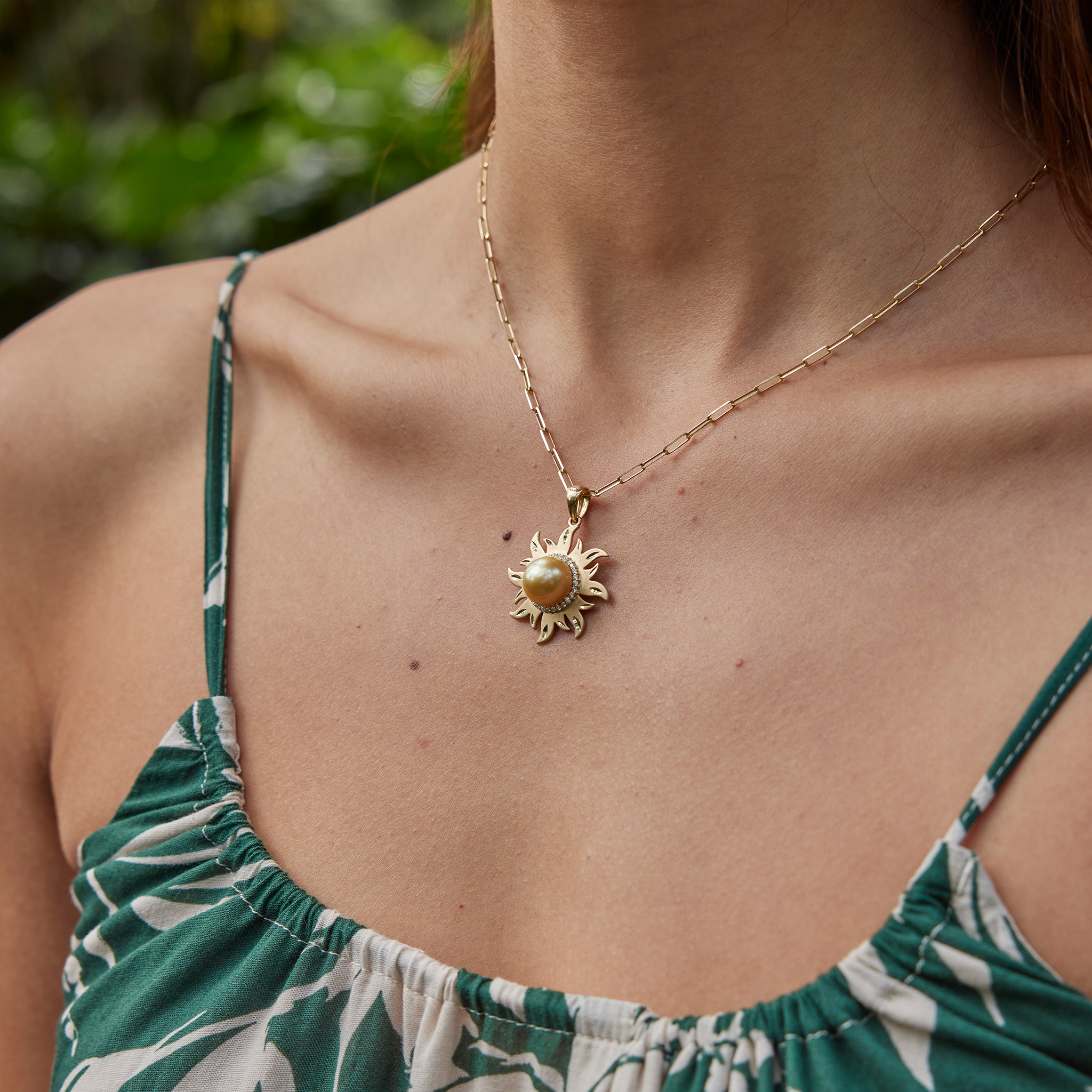Side view of a Diamond South Sea gold pearl sun pendant in 14k yellow gold on a paperclip chain, worn by a woman in a green patterned top.