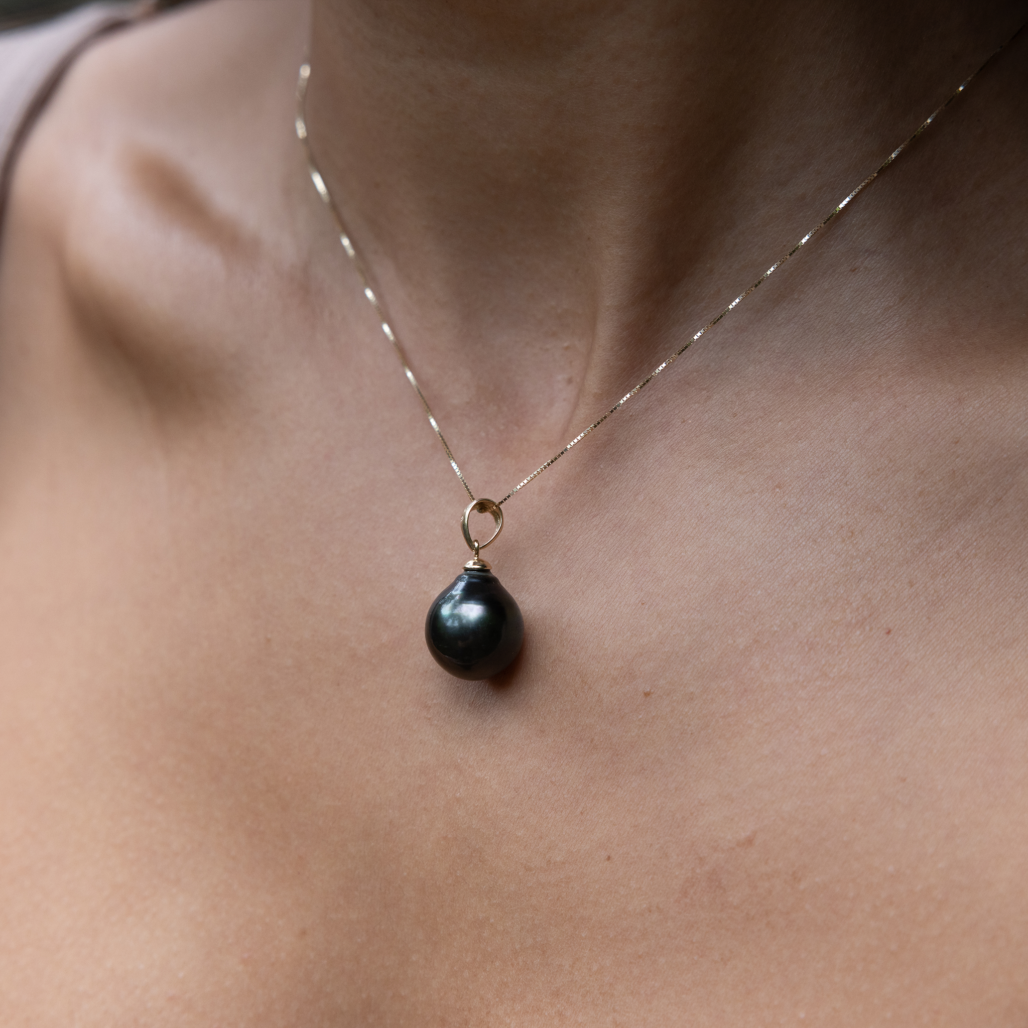 Close-up of a woman wearing a drop-shape Tahitian black pearl pendant.