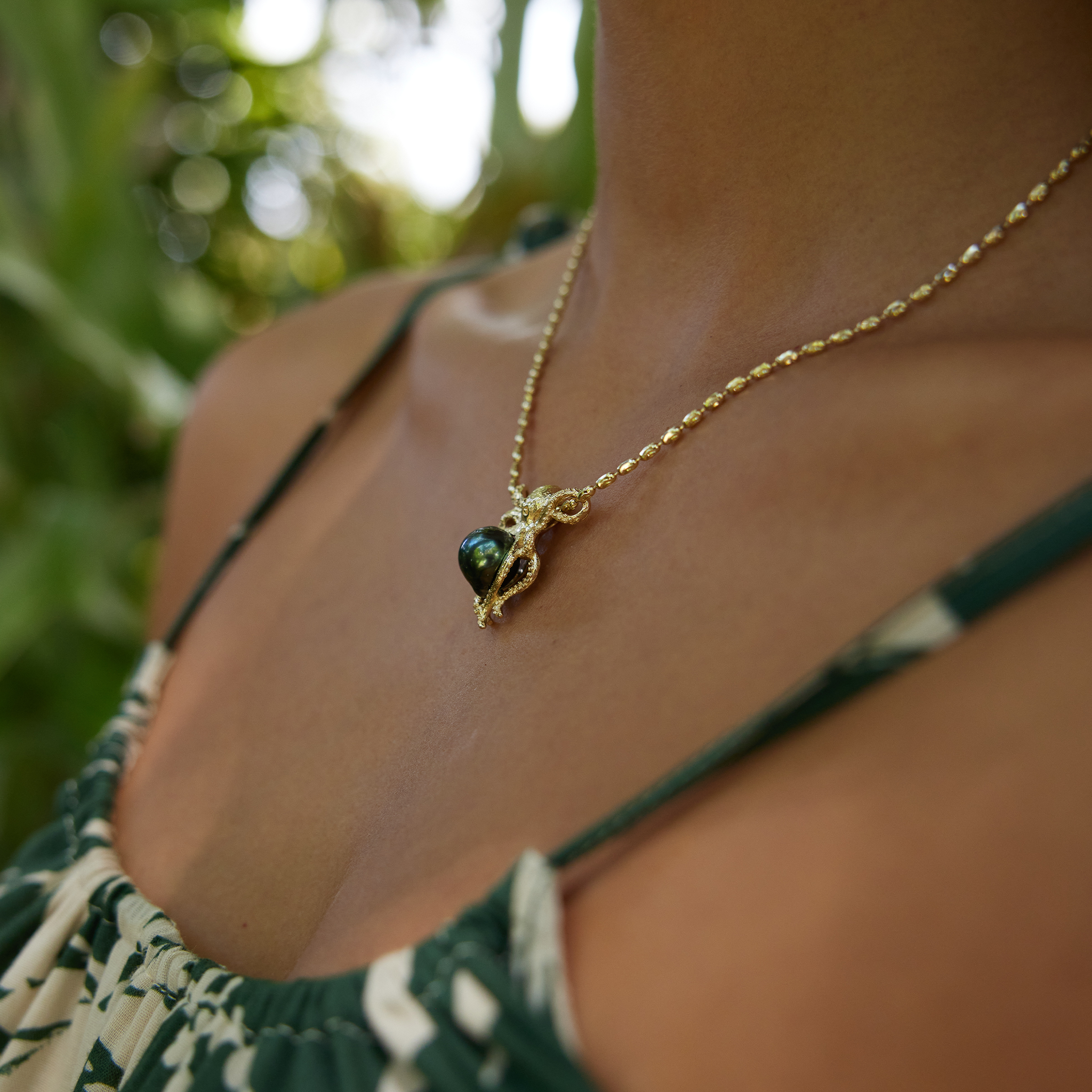 Close-up of a person wearing a Octopus Tahitian black pearl pendant in 14k yellow gold from the side.