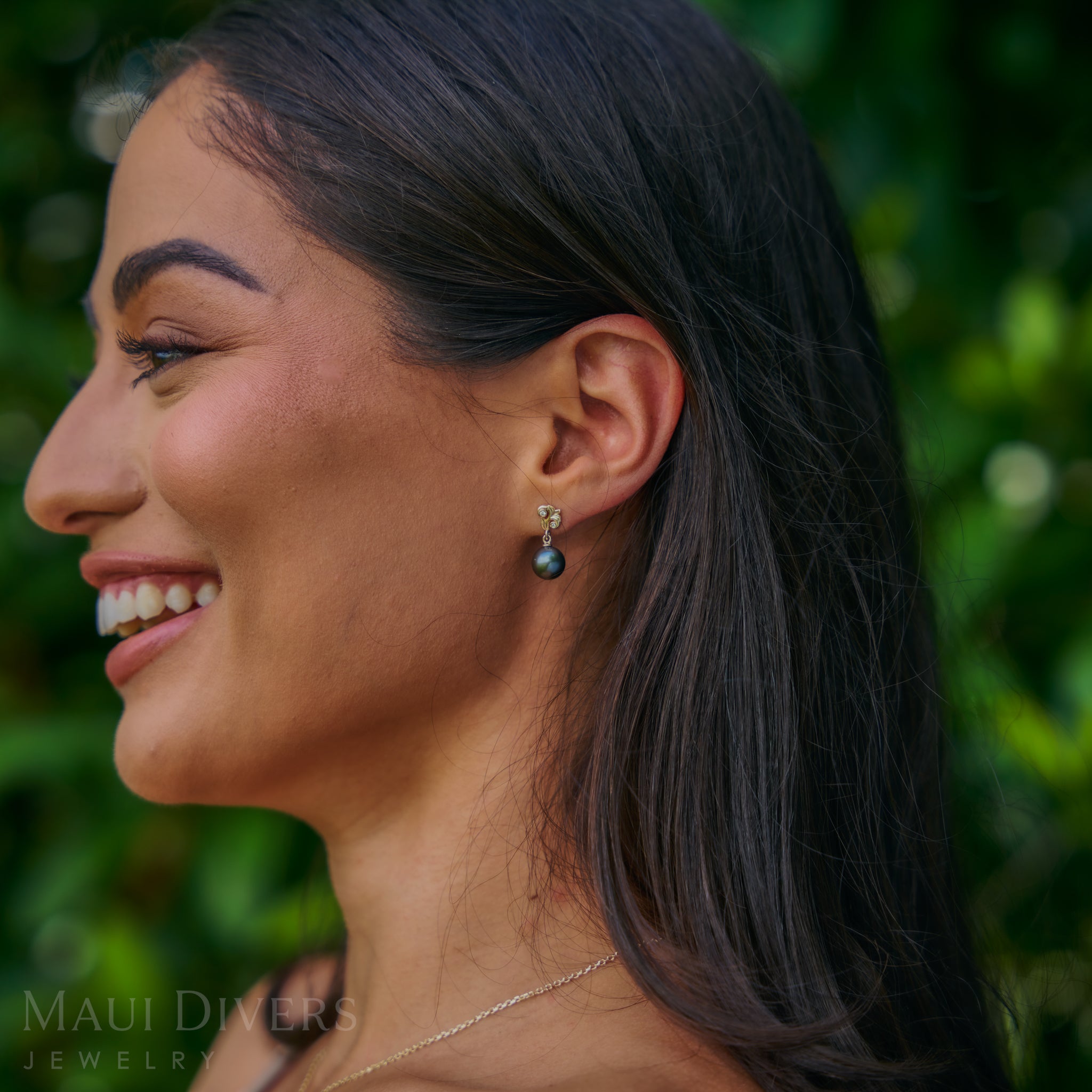 A woman wearing a black pearl earring with a blurred green background.