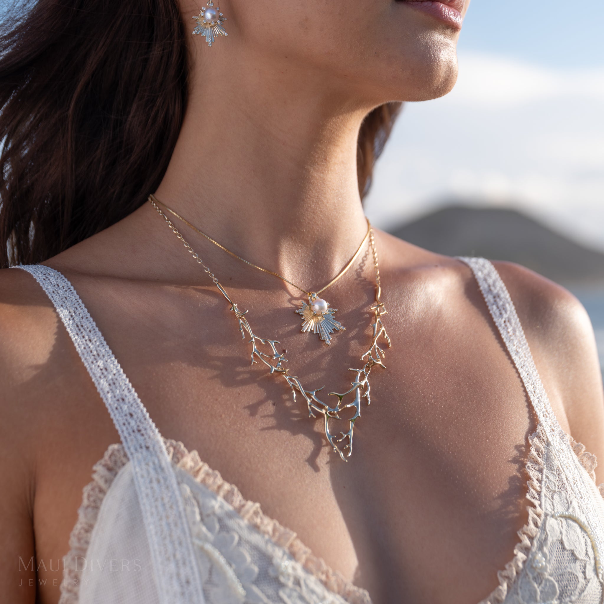 Close-up of a woman wearing an sunrise-inspired diamond and akoya white pearl pendant in yellow gold, layered with the yellow gold Heritage Collection necklace