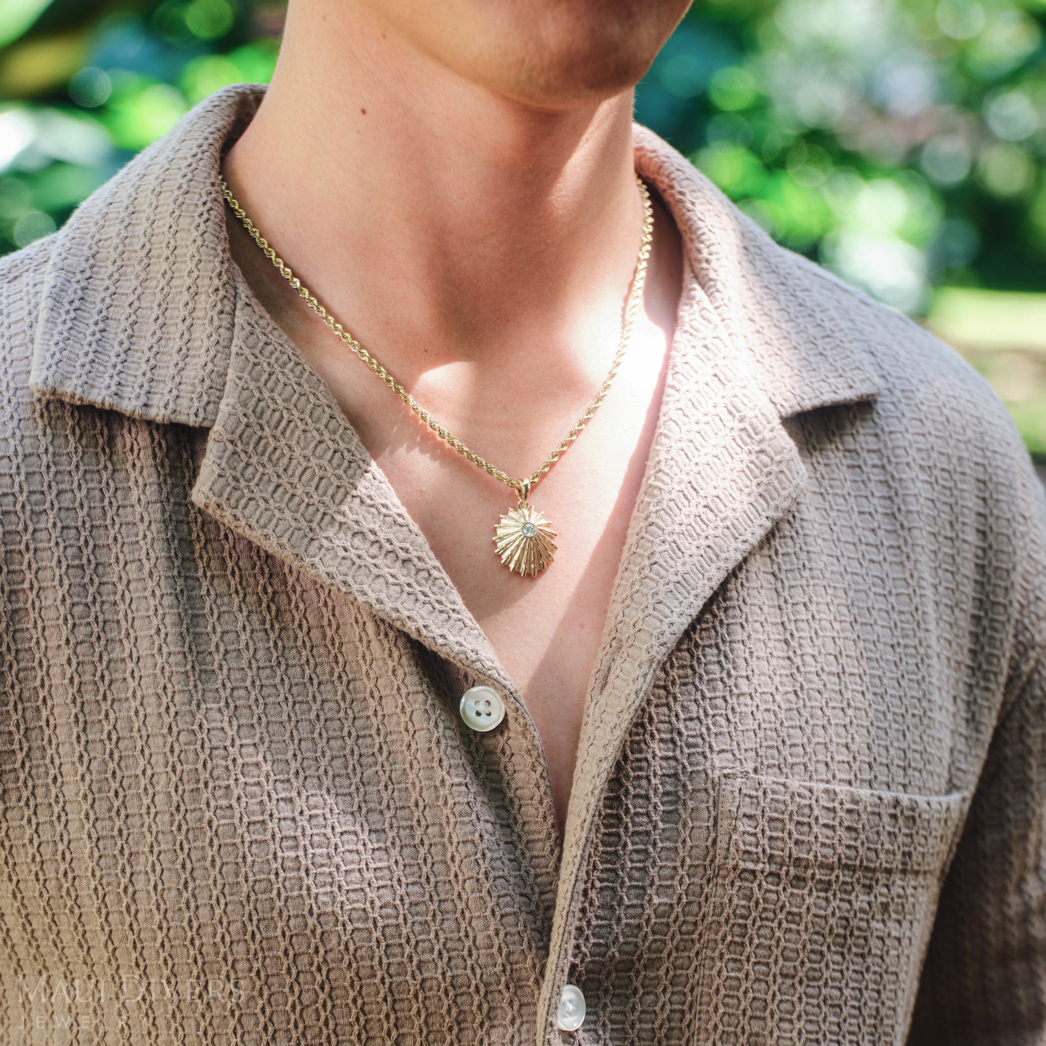 Close-up of a man in a brown shirt wearing a ʻOpihi Pendant in 14k yellow gold with a lab grown diamond, against a blurred background
