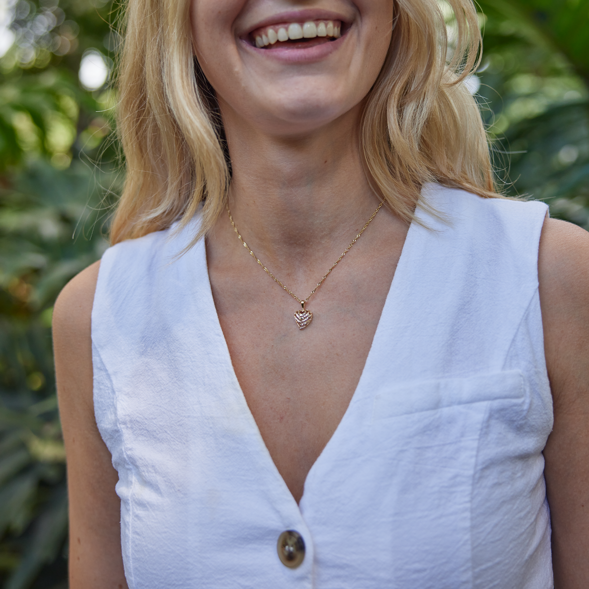 Woman in white wearing gold Aloha Heart Pendant with cut-out design spelling "Aloha"
