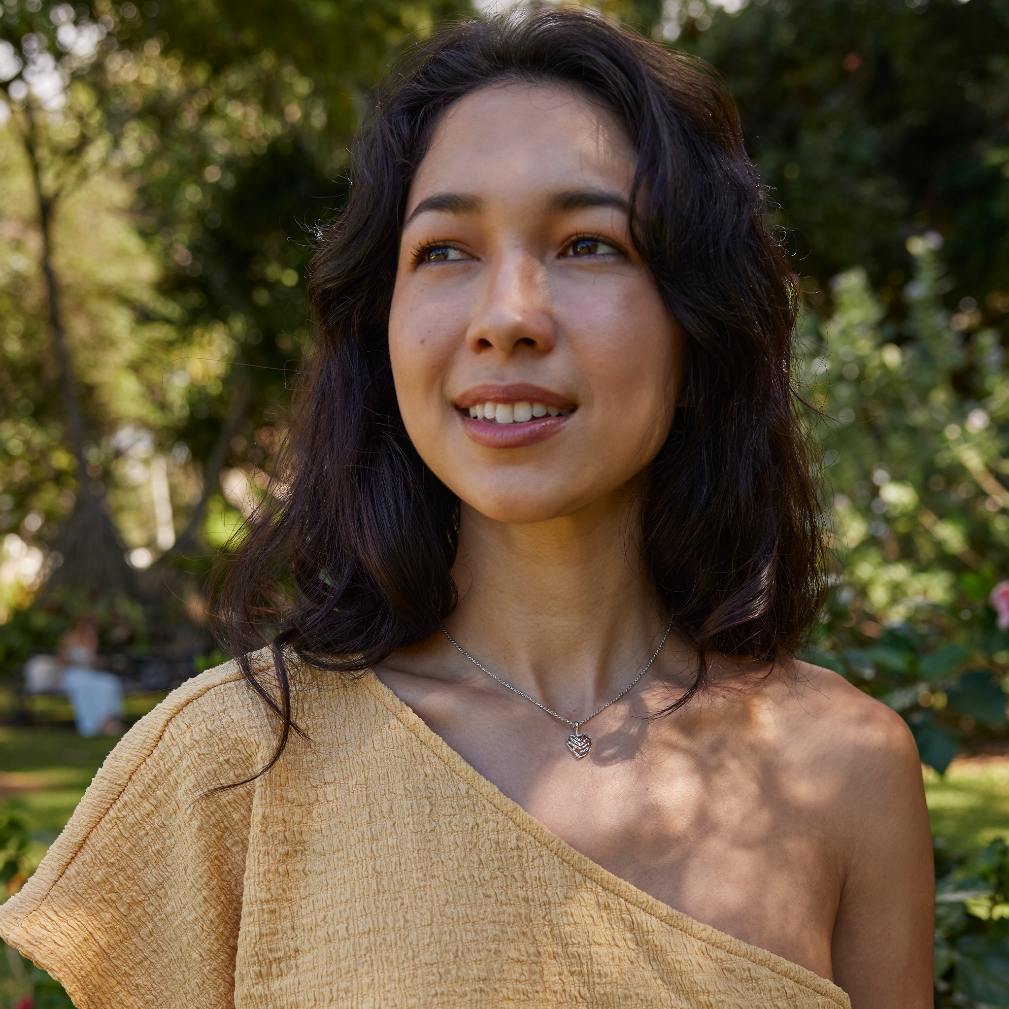 Young woman in lush garden wearing white gold Aloha Heart Pendant with cut-out design spelling "Aloha"