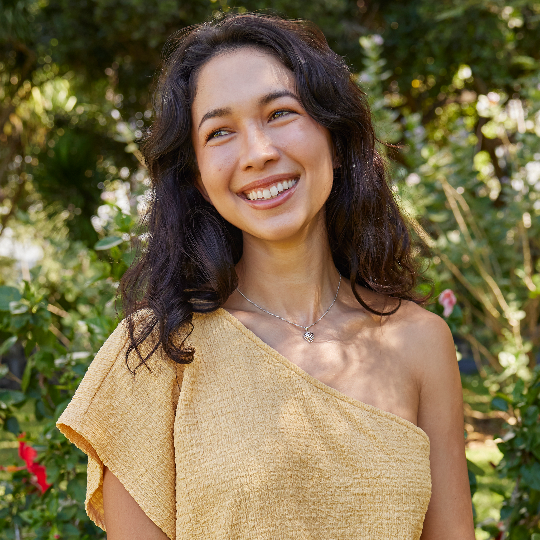 Young woman in lush garden wearing white gold Aloha Heart Pendant with cut-out design on chain