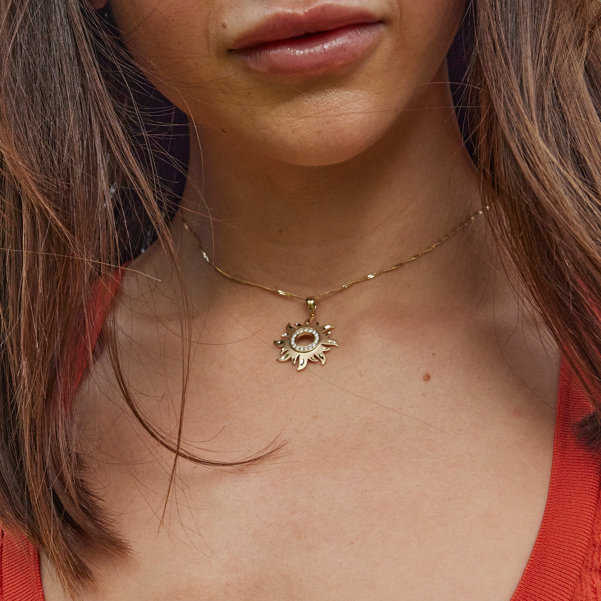 Woman's neckline wearing a gold sun pendant with diamonds and diamond-cut accent