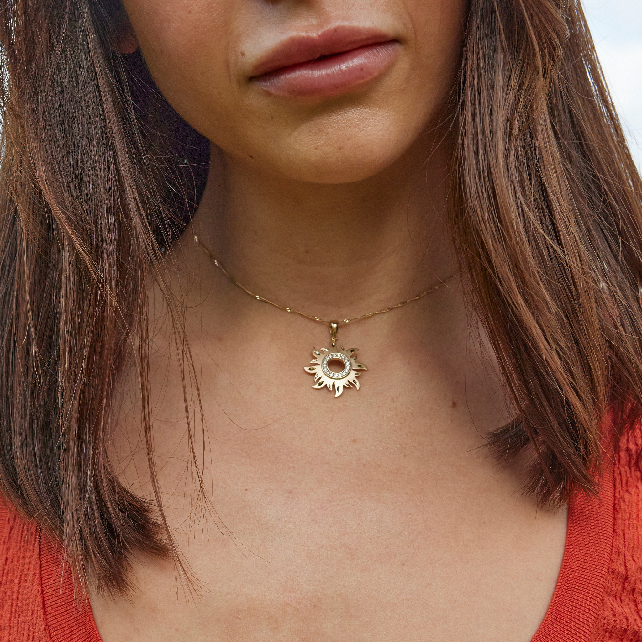 Close up of woman's neckline wearing a gold sun pendant with diamonds at the center
