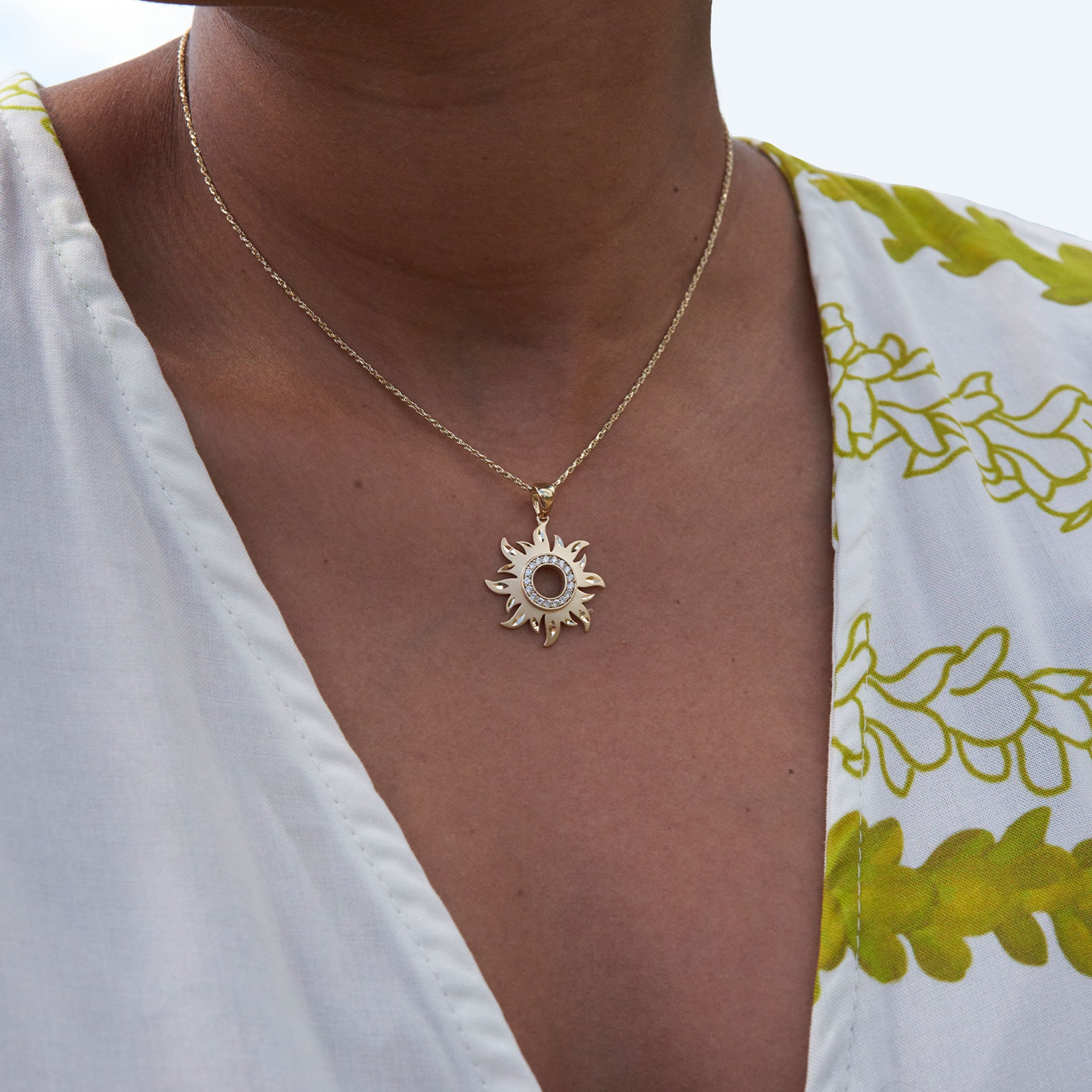 Close up of a neckline wearing a gold sun pendant with diamonds on a chain
