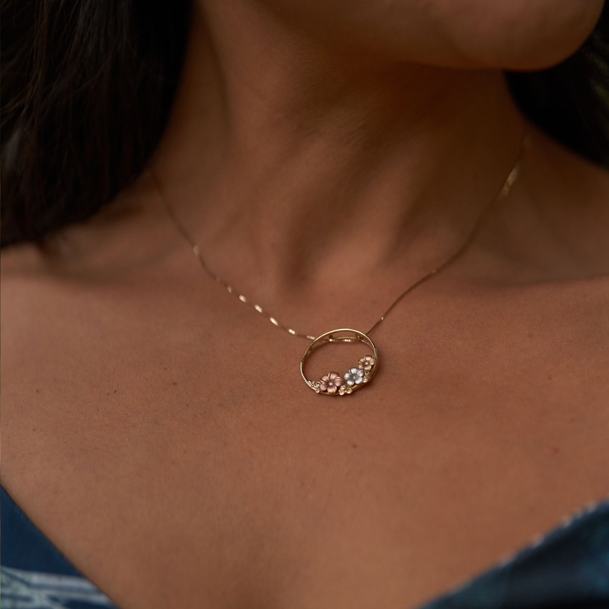 Close up of woman's neckline wearing a circle shaped pendant adorned with plumeria and diamond details