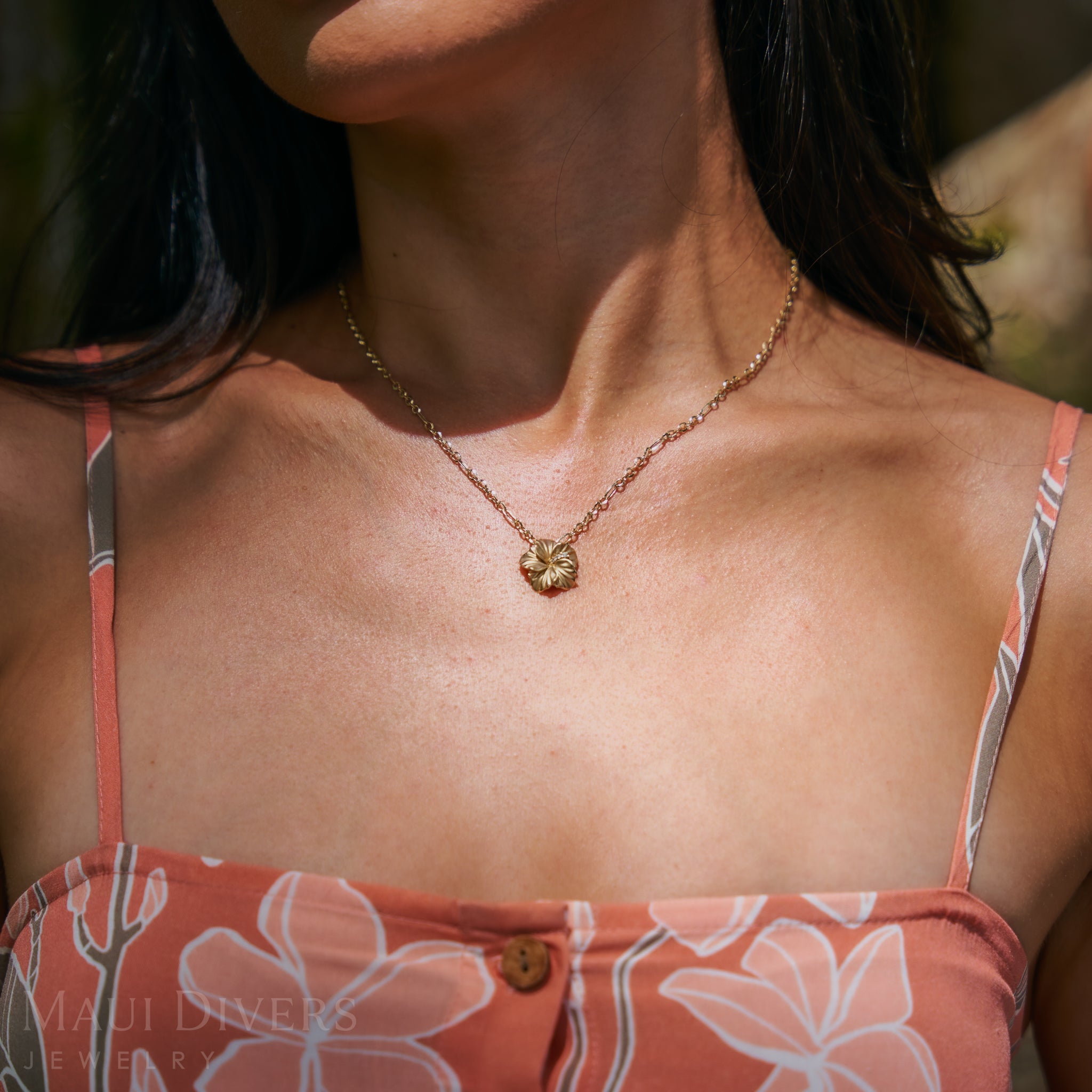 Close-up of a diamond hibiscus pendant worn by a person with a floral top.
