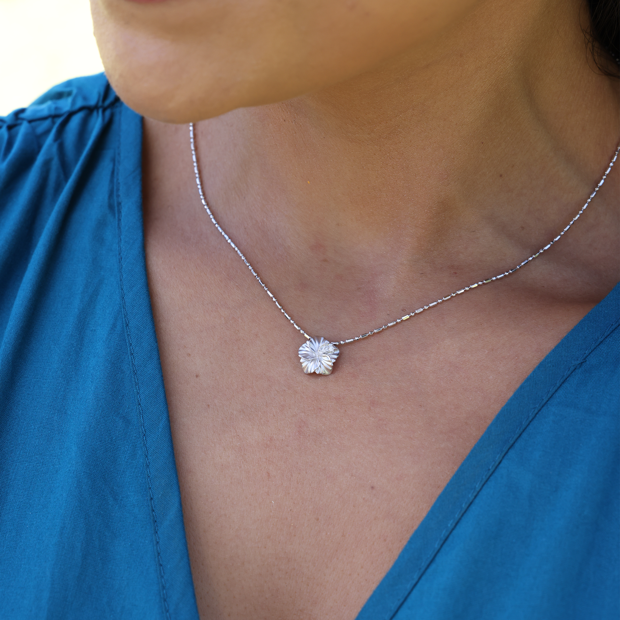 Close up of woman in blue top wearing white gold hibiscus pendant on chain