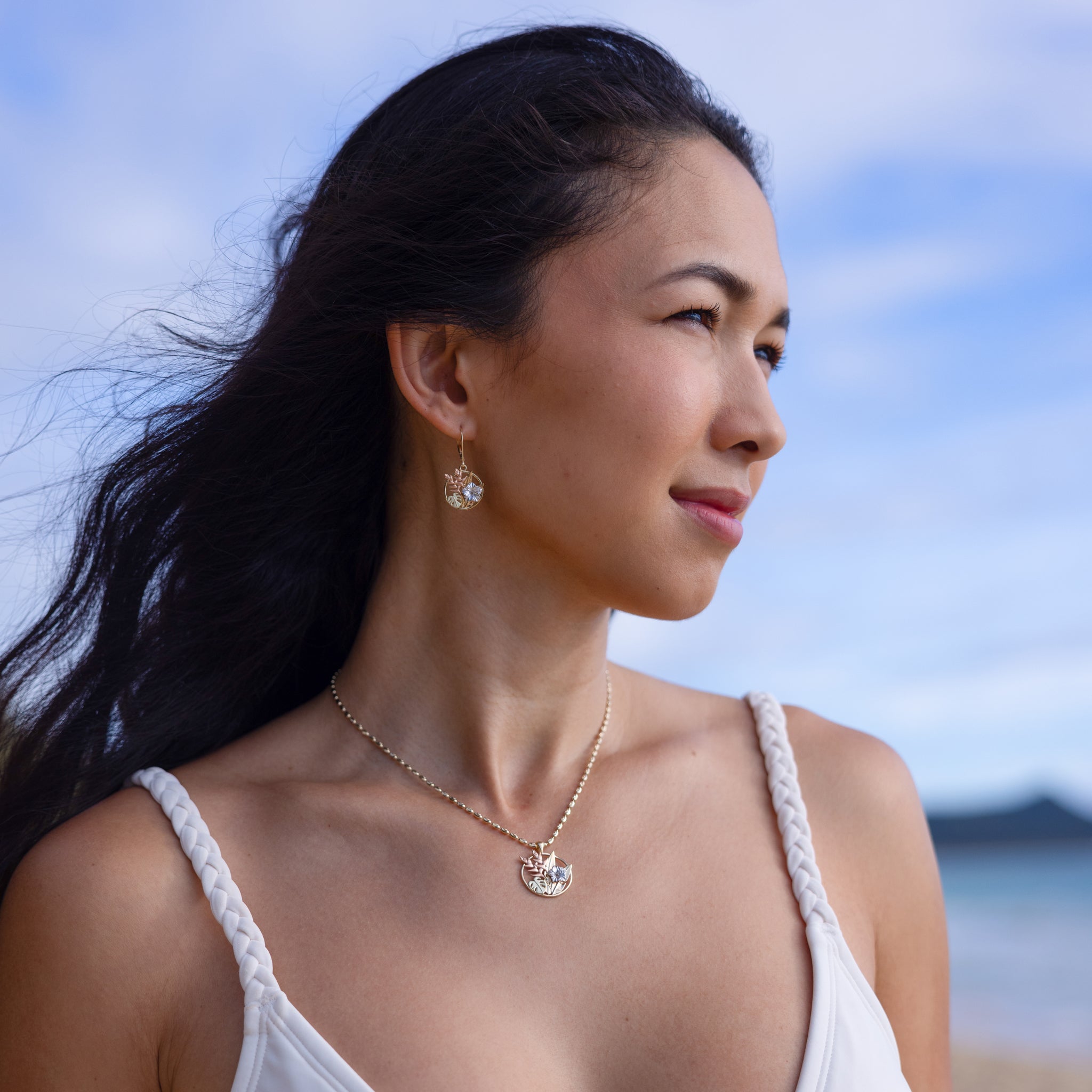 Woman wearing Hawaiian Gardens Pendant and Earrings in four tone gold with diamonds on beach