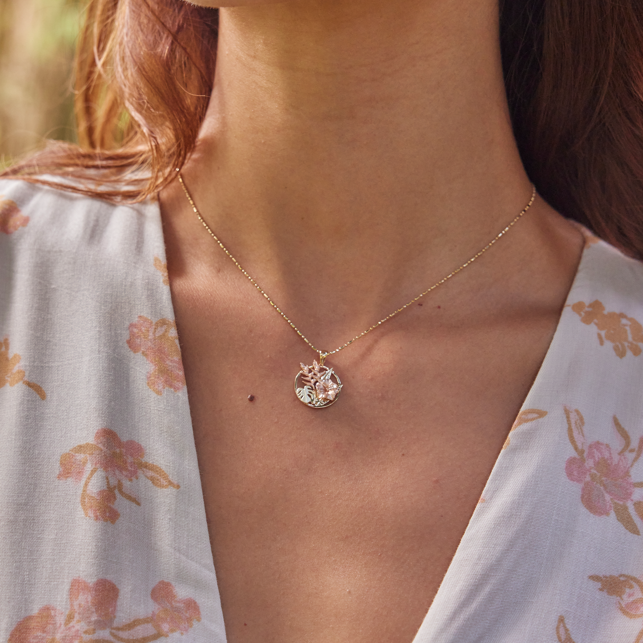 Close up of woman wearing Hibiscus, Heliconia and Monstera Pendant in Tri-color gold with diamonds