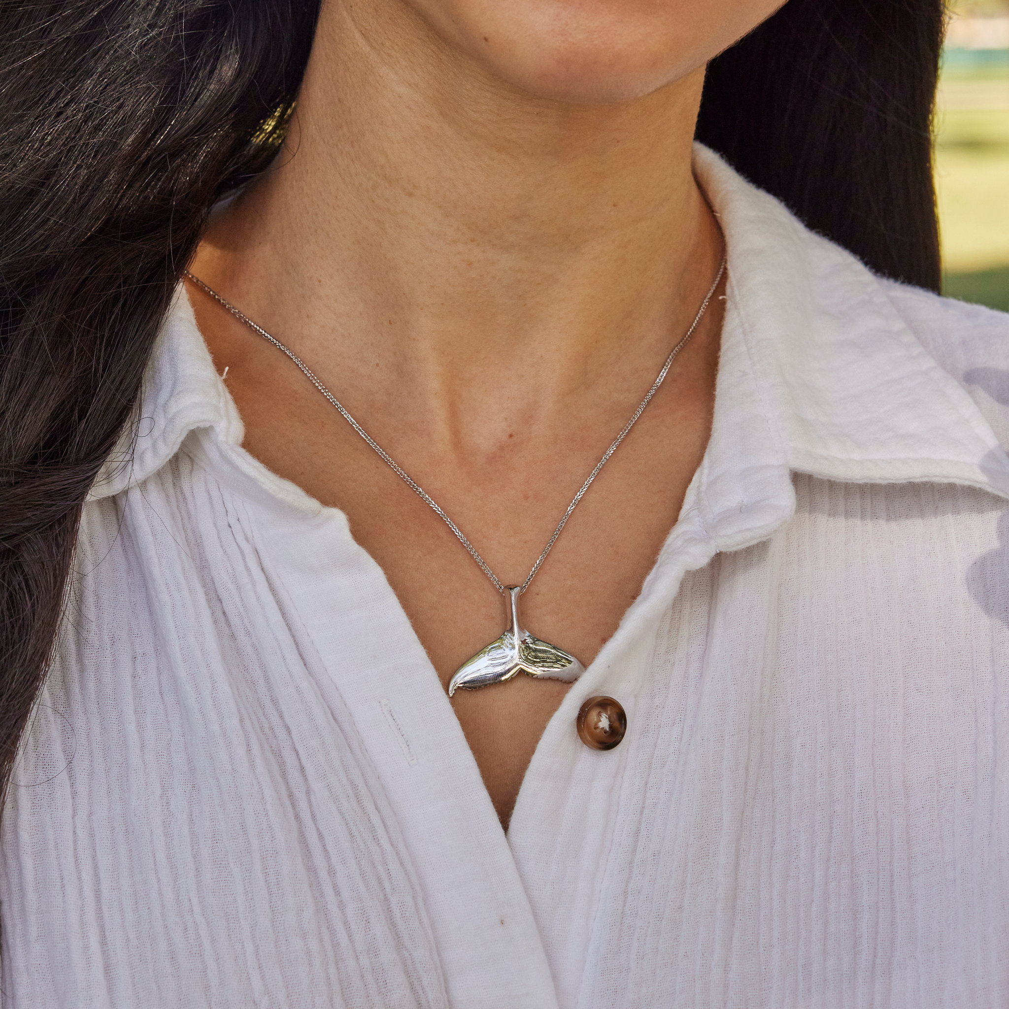 Woman wearing a white shirt with a whale tail pendant in white gold