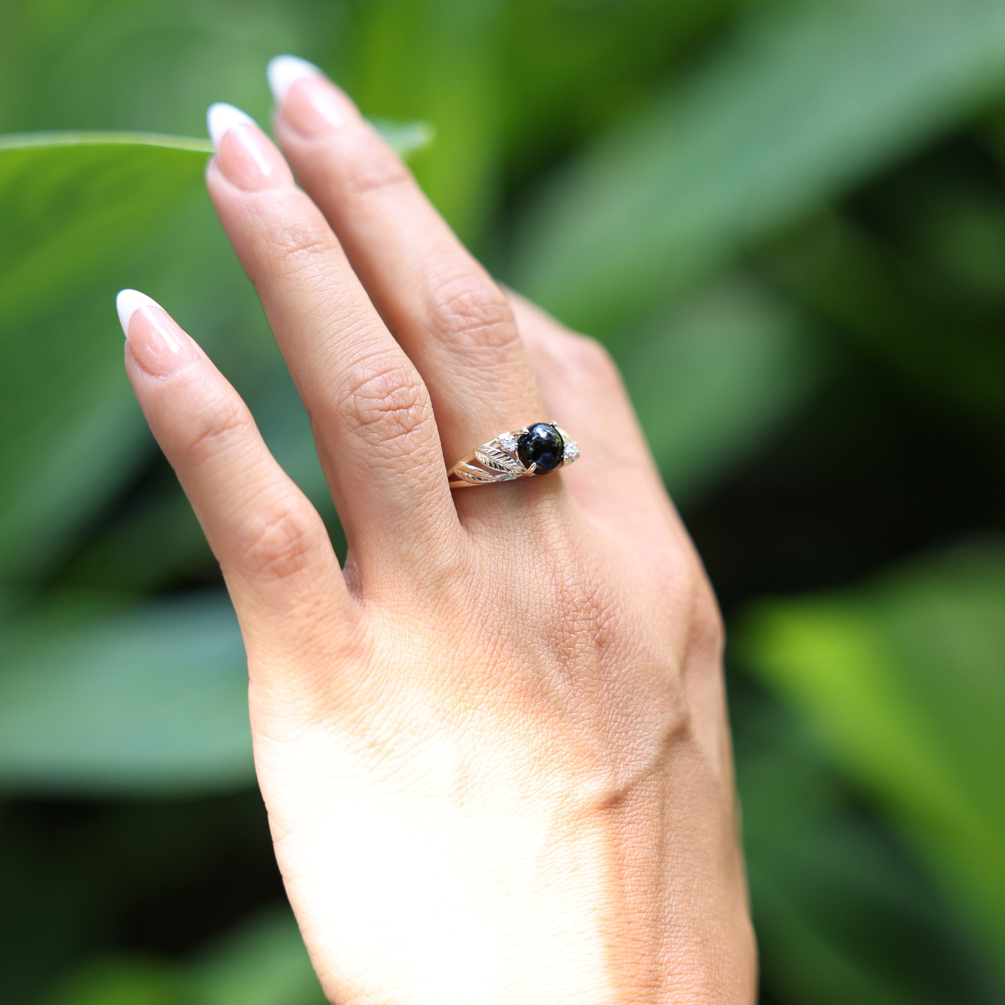 Woman wearing Maile Hawaiian Black Coral Ring in Gold with Diamonds while touching leaf