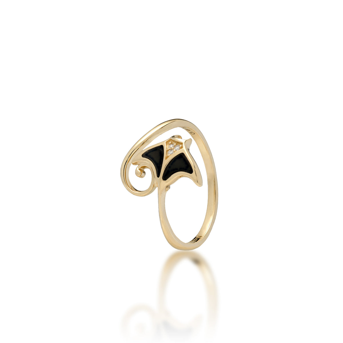 A 12mm Sealife Manta Ray ring in 14k gold, the fins are inlayed with Hawaiian Black Coral with diamonds details on the head, the tail curves around forming the band of the ring, placed on a reflective white surface.
