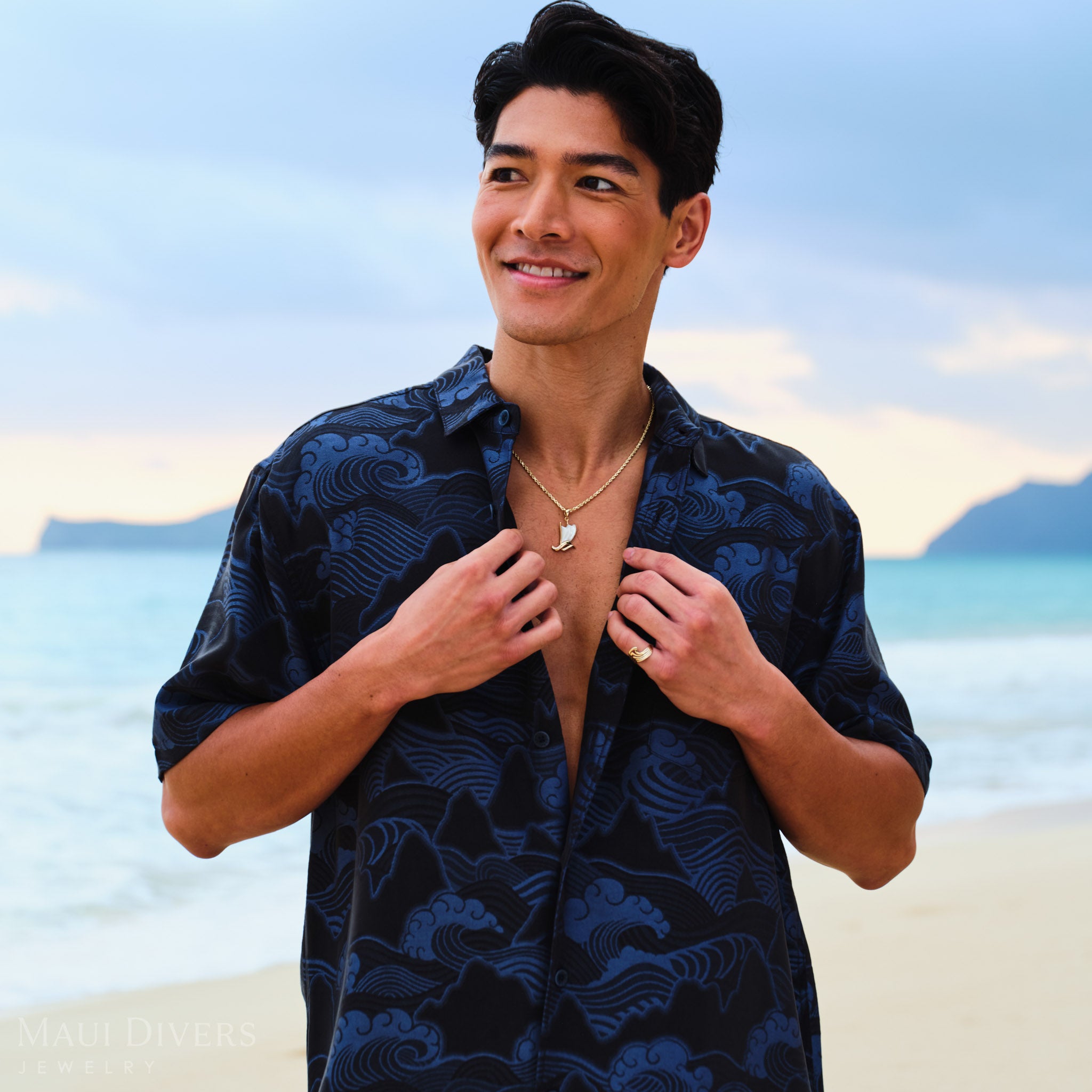 Waʻa (Canoe) Pendant on a gold chain worn by a man in a blue patterned shirt on a beach