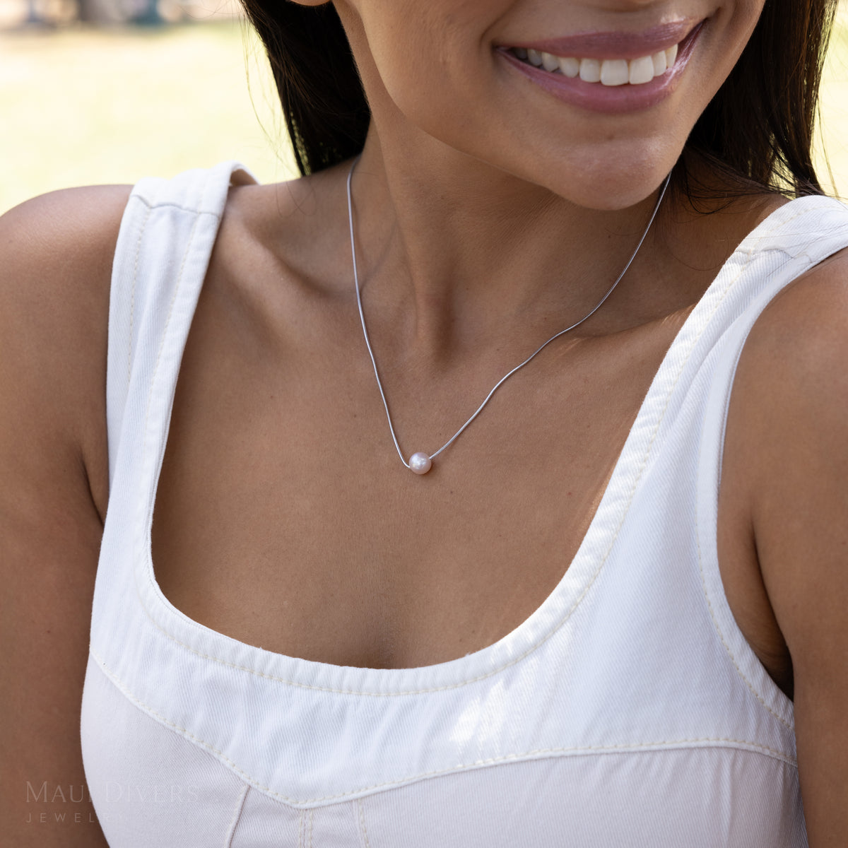 A close-up lifestyle shot of a woman wearing a delicate silver chain necklace with a single white pearl pendant, styled with a white sleeveless top.