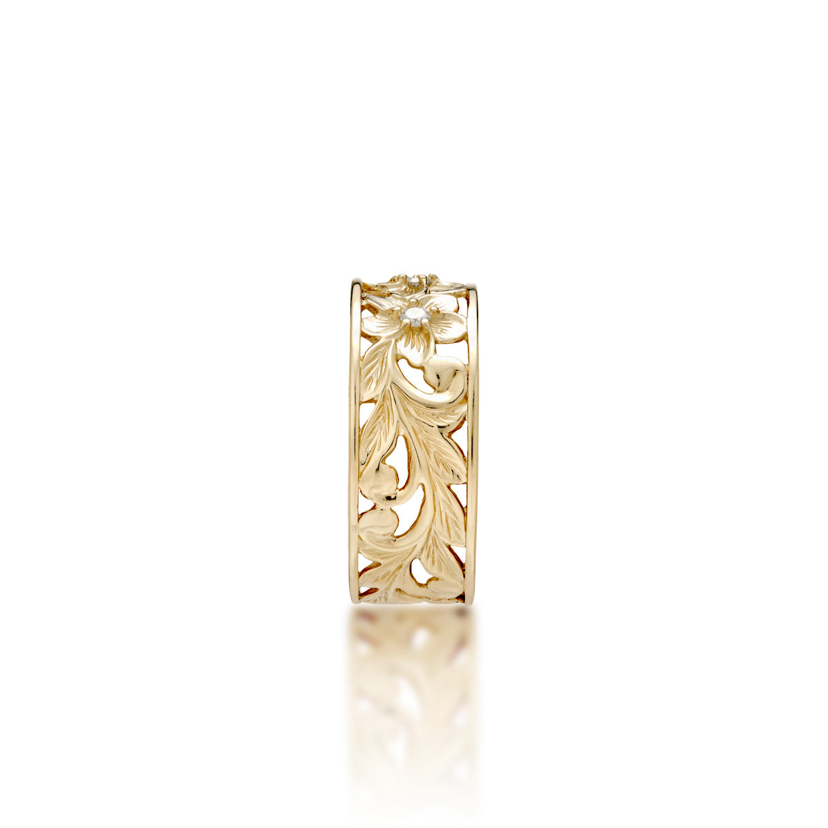 A side view of a 14k yellow gold Hawaiian Heirloom ring with an intricate fern and maile leaf scrollwork pattern featuring plumeria flowers at the top with diamond accents, shown on a clean white background with a soft reflection.