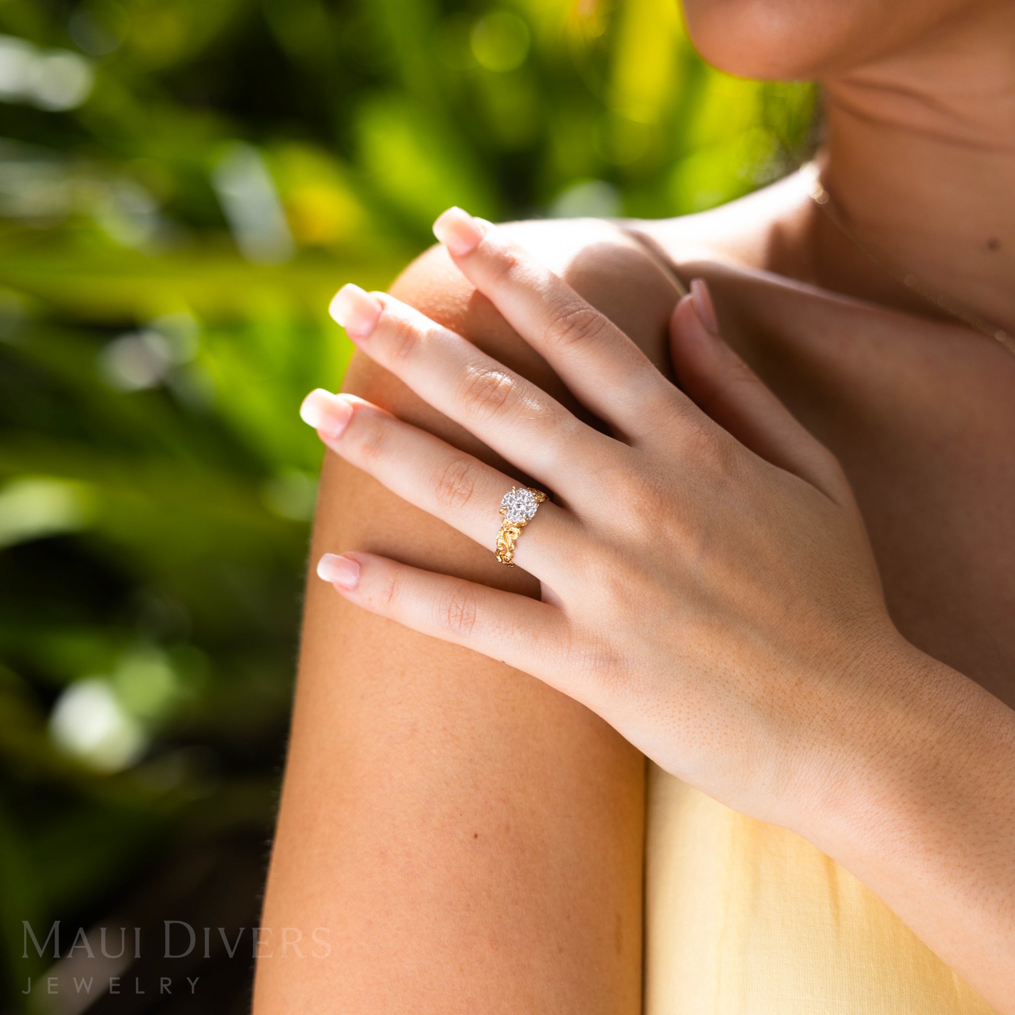 Close-up of a hand wearing Living Heirloom Engagement Ring in Gold with Diamonds against a green background