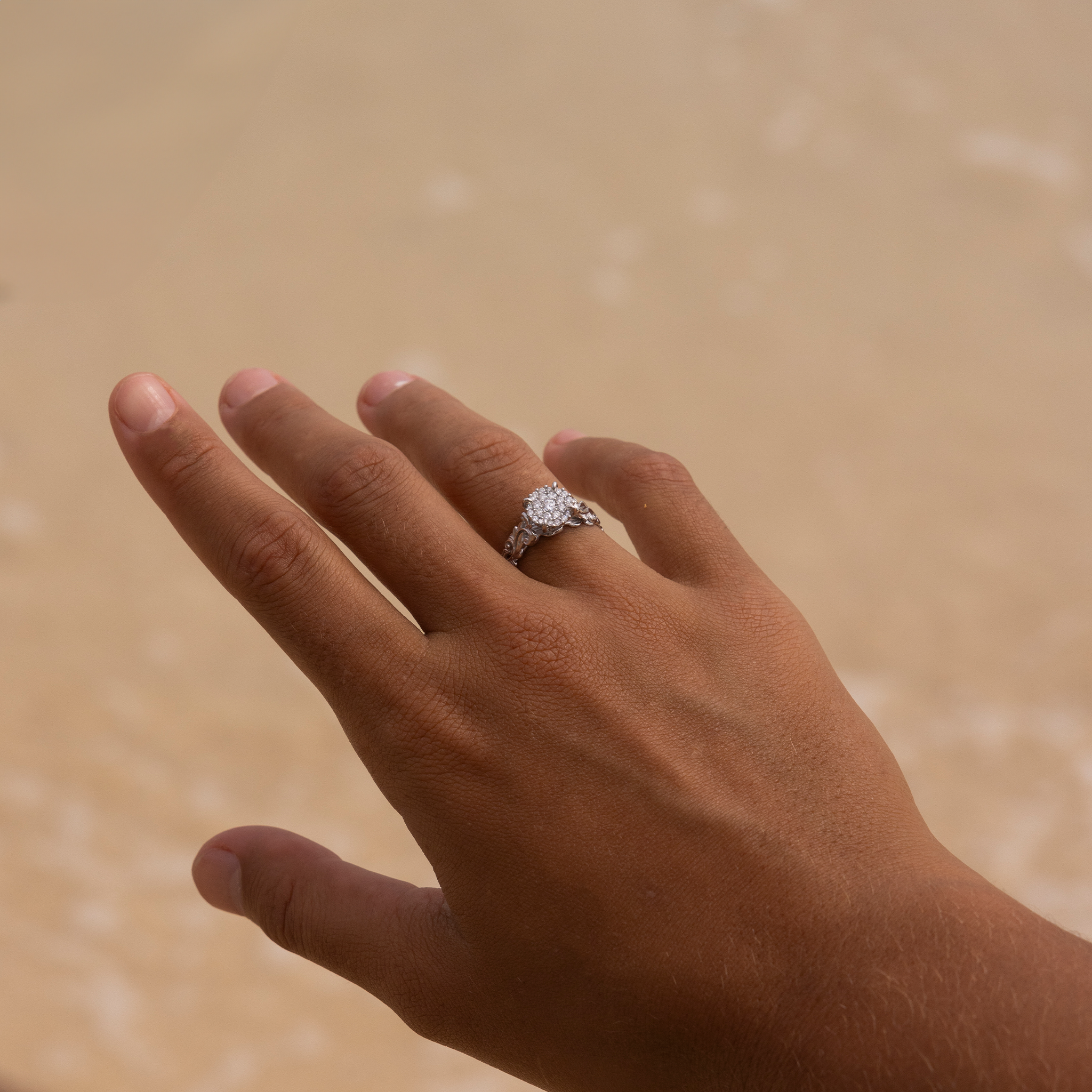 Woman's hand wearing Living Heirloom Engagement Ring in White Gold with Diamonds against sand