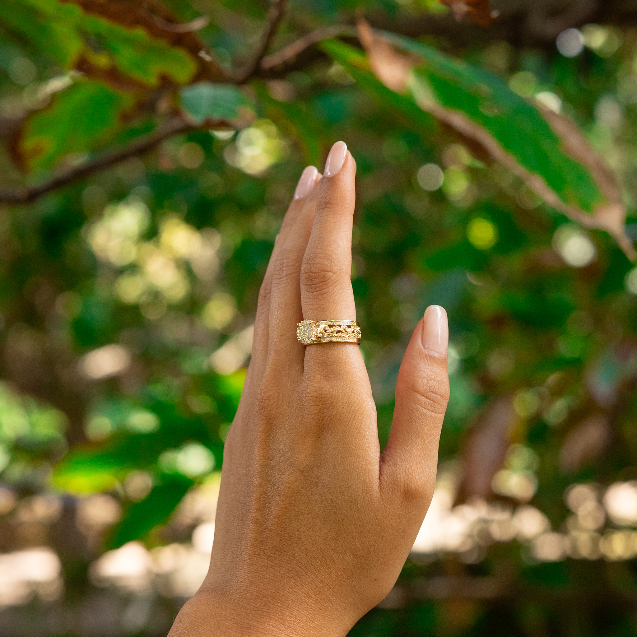 Woman's hand wearing a Living Heirloom Engagement Ring in Gold with Diamonds with a blurry green background