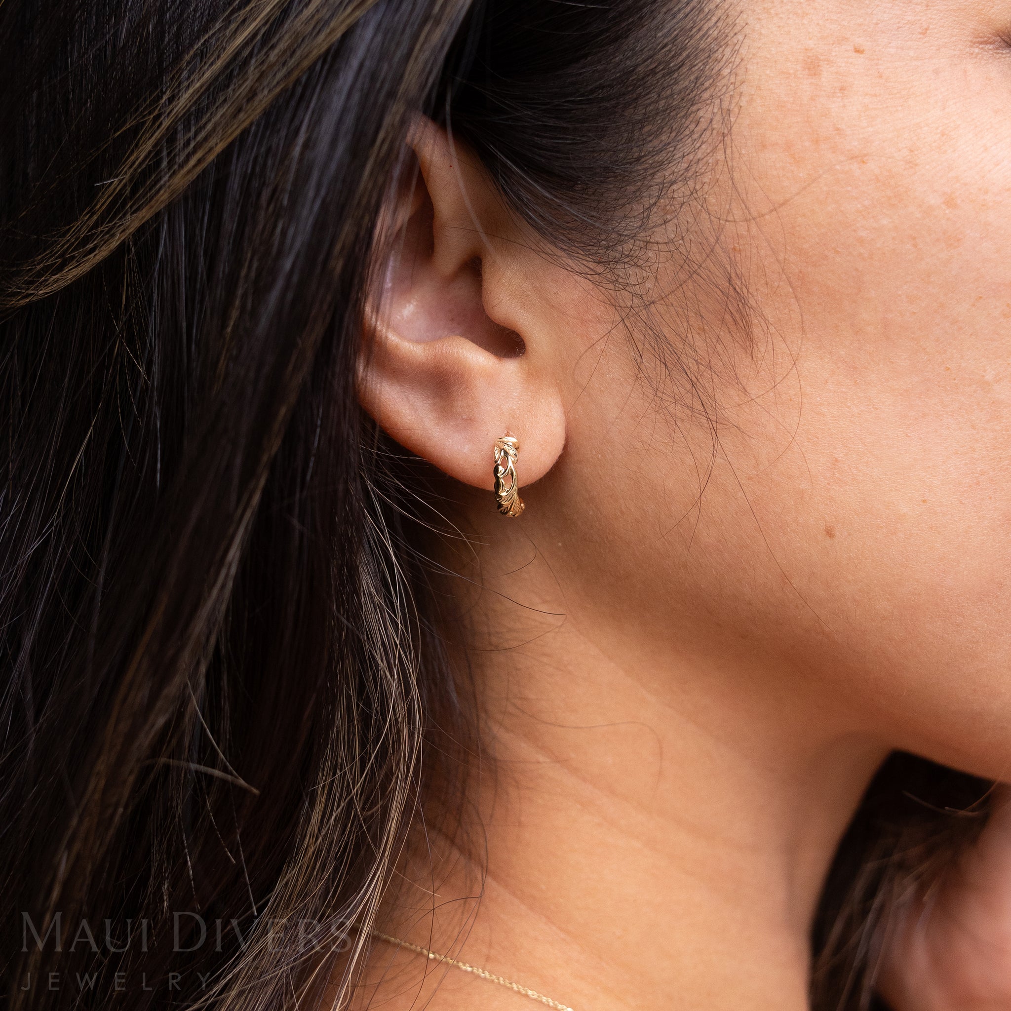 Close-up of a woman wearing a Hawaiian Heirloom Old English Scroll Earrings in 14k yellow gold on her ear