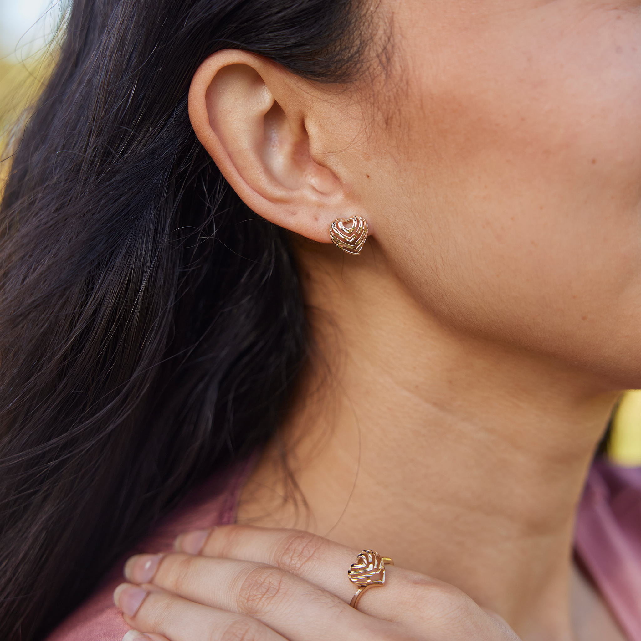 Close up of woman wearing 11mm Aloha Heart Earrings and Ring in Gold