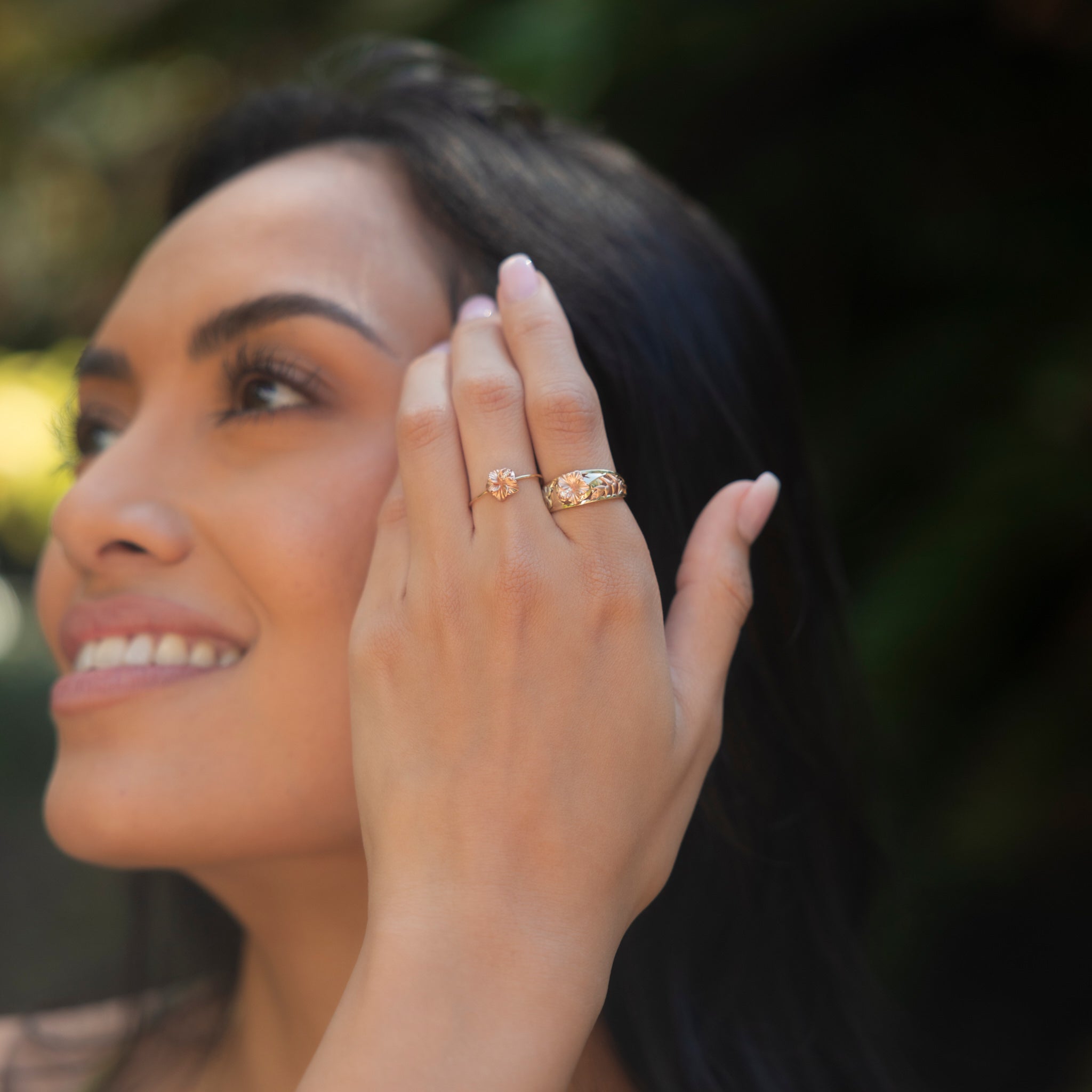 Two Hawaiian Gardens Hibiscus Rings in Gold with Diamonds on a womanʻs hand touching her hair