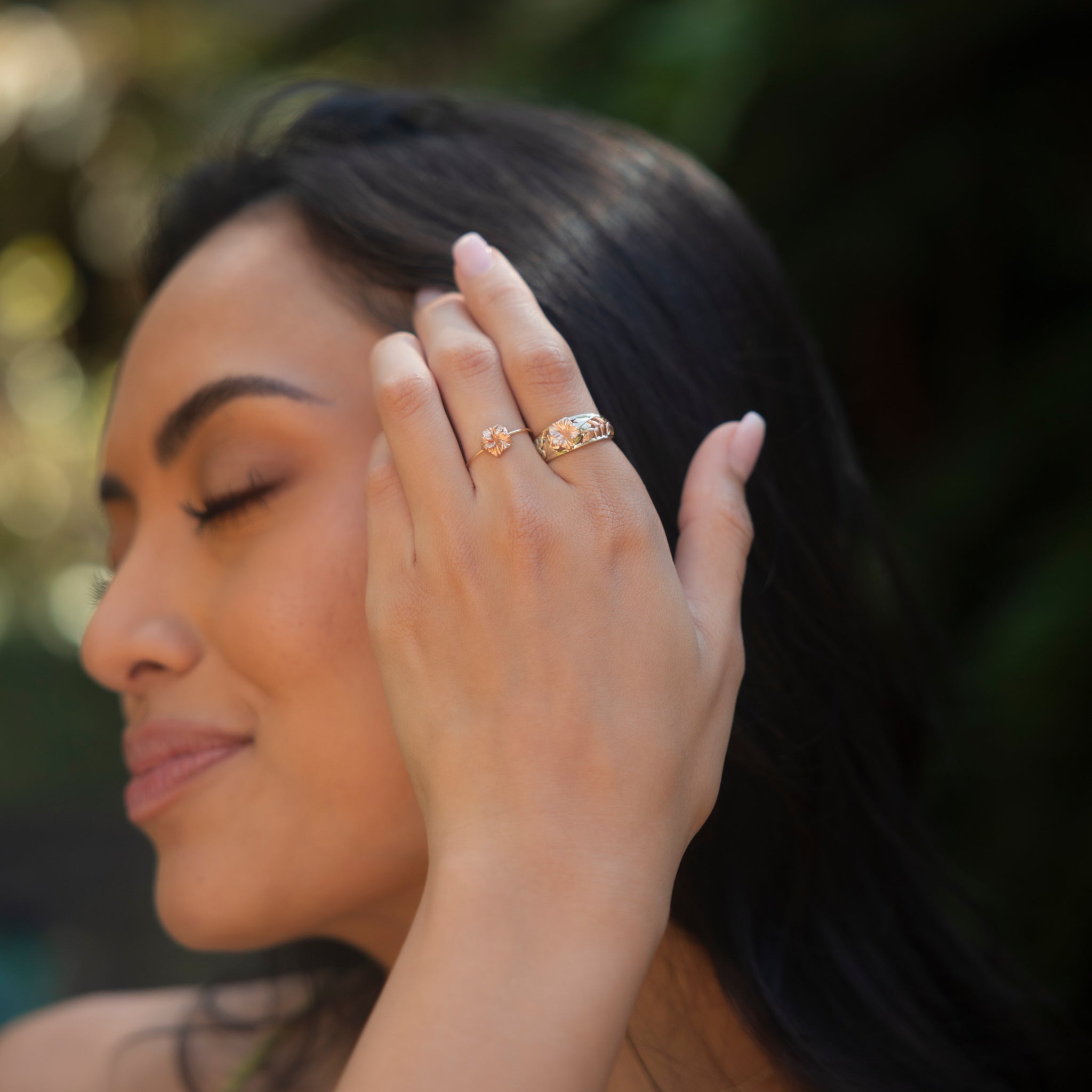 Two Hawaiian Gardens Hibiscus Rings in Gold with Diamonds on a womanʻs hand touching her hair