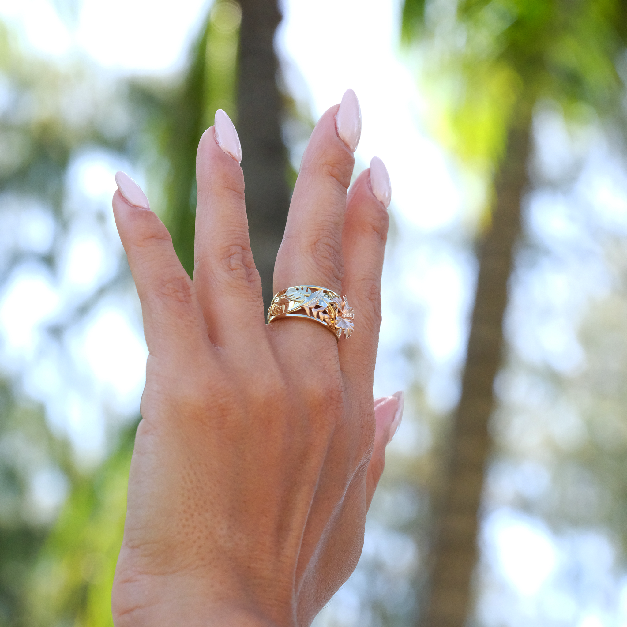A woman's hand with a Hawaiian Gardens Hibiscus Ring in Tri Color Gold with Diamonds - 12mm - Maui Divers Jewelry