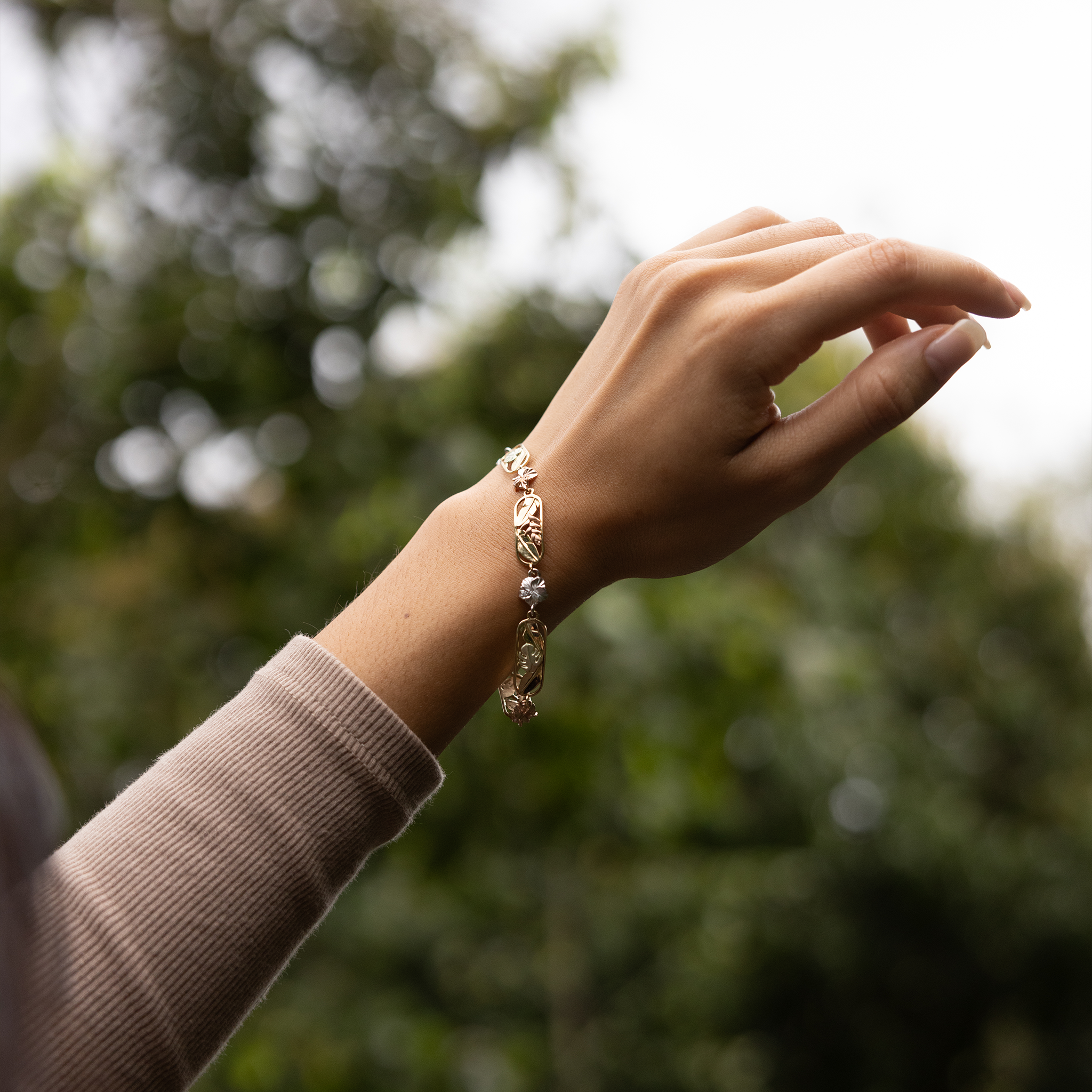 Hawaiian Gardens Link Bracelet in Yellow, White, Rose and Green Gold with Diamonds on a wrist up against greenery