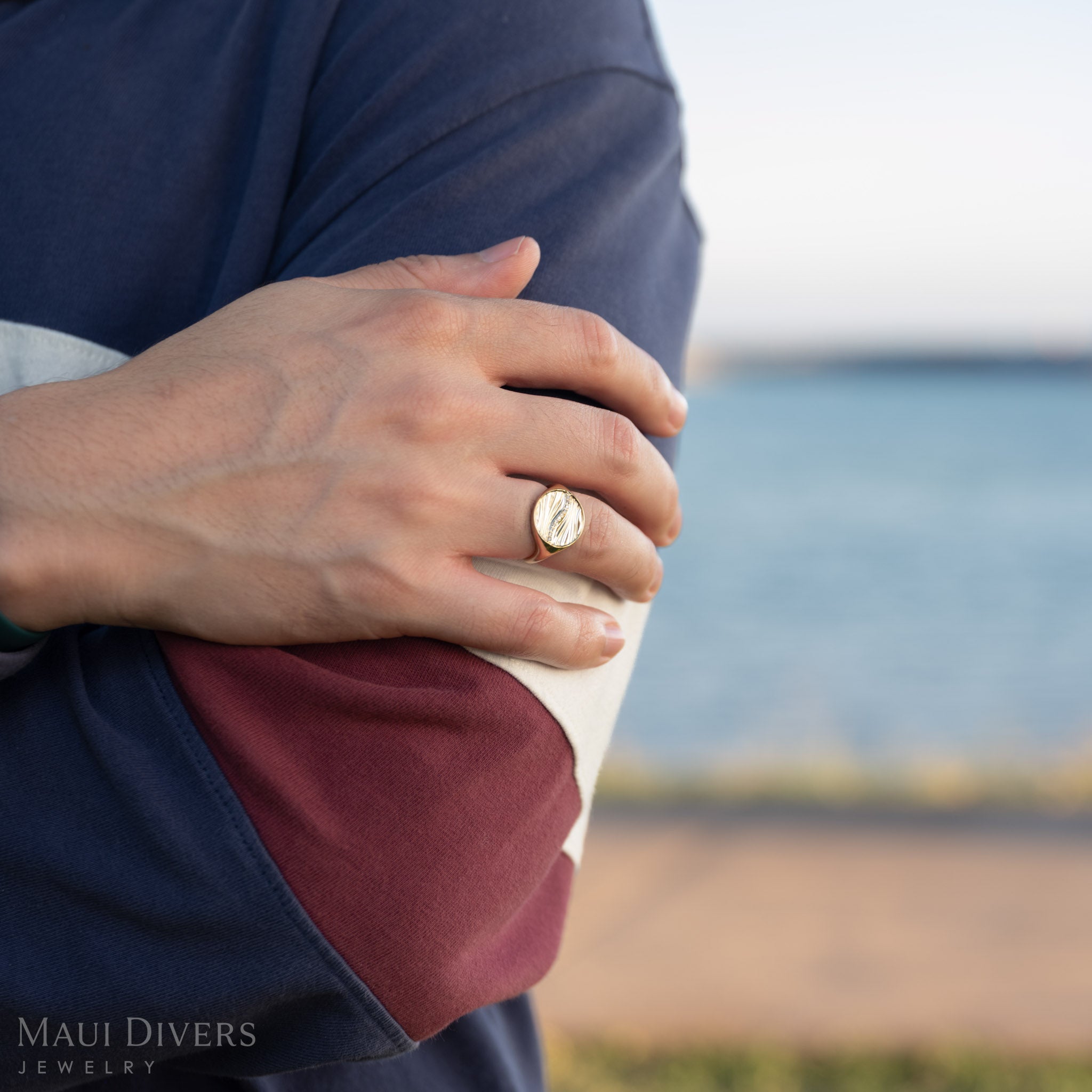 Man wearing a gold ocean sand signet ring with a blurred ocean background