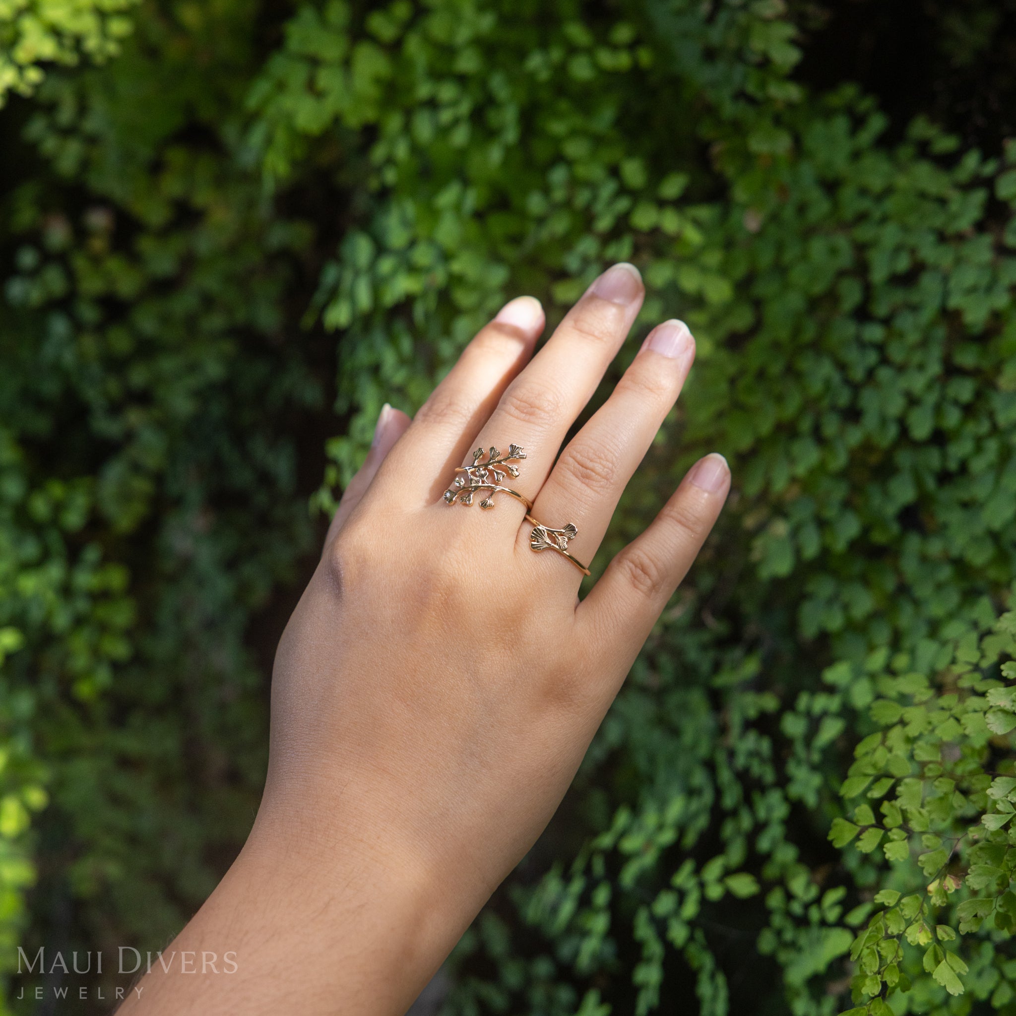 Hand wearing an 18mm and 10mm 14k Yellow Gold Maiden Hair Ring with blurry Maiden Hair ferns in the background