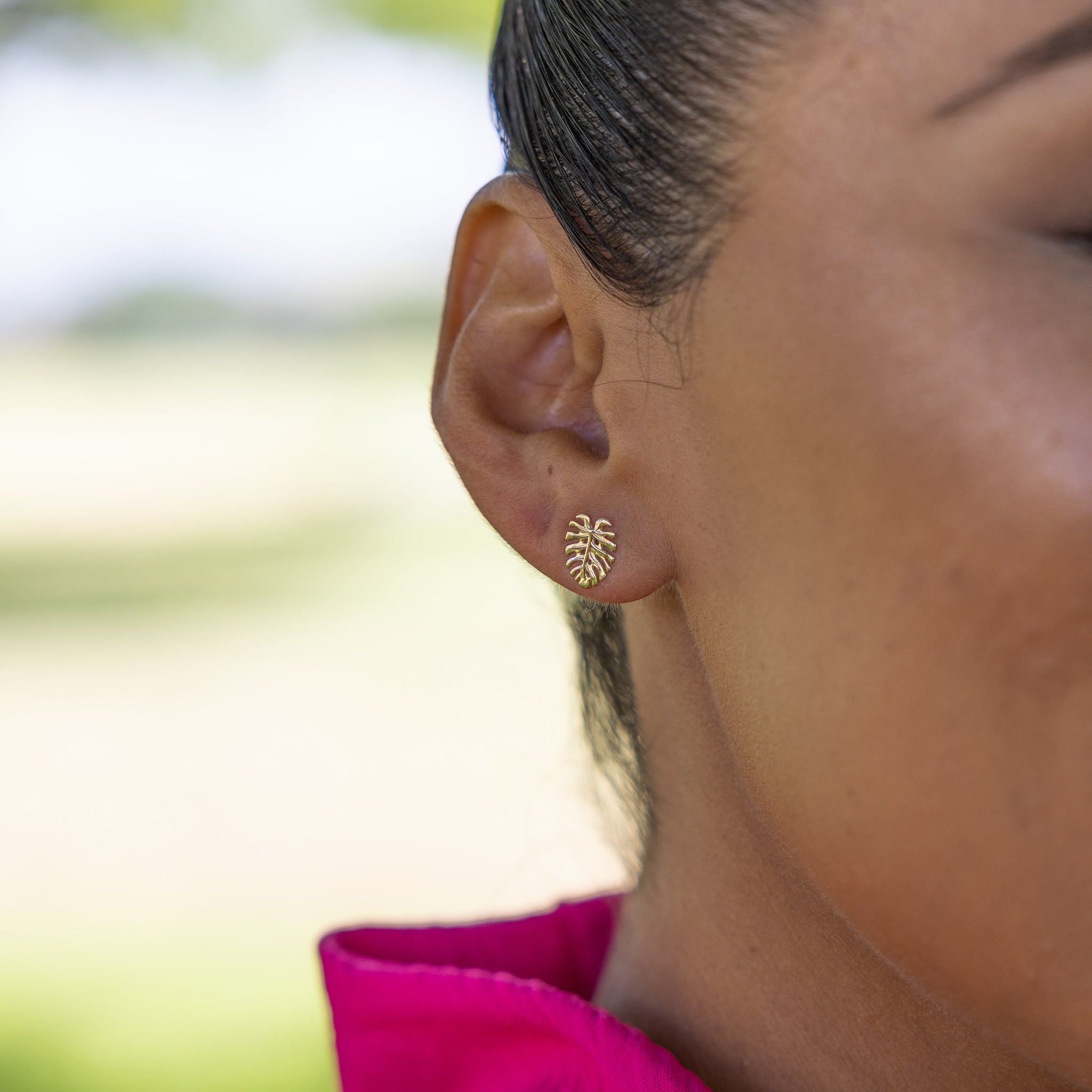 Close up of 9mm Monstera Earrings in Gold on ear with bright blurred background
