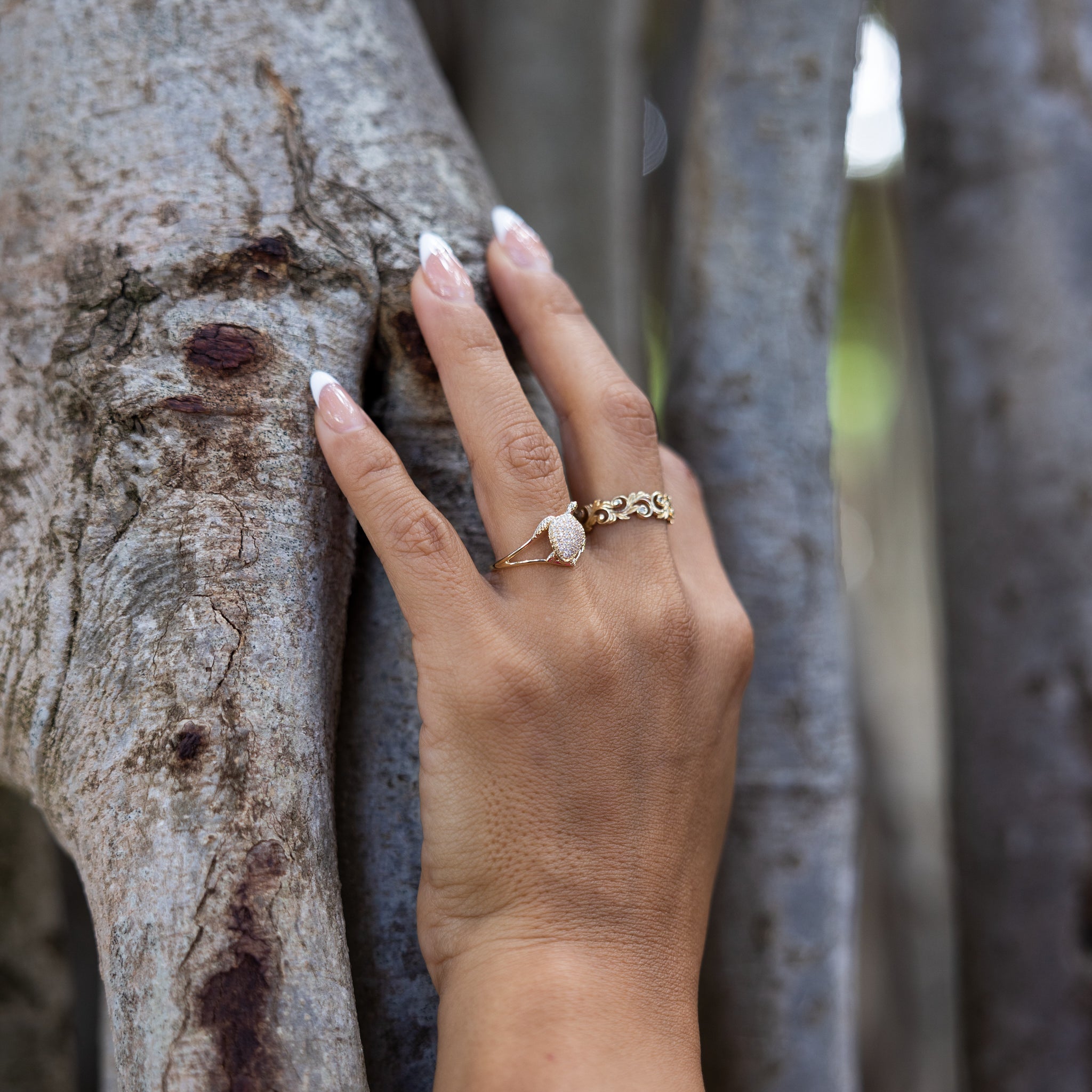 A woman's hand wearing a Living Heirloom Ring in 14k Yellow Gold with Diamonds and a honu ring on a tree