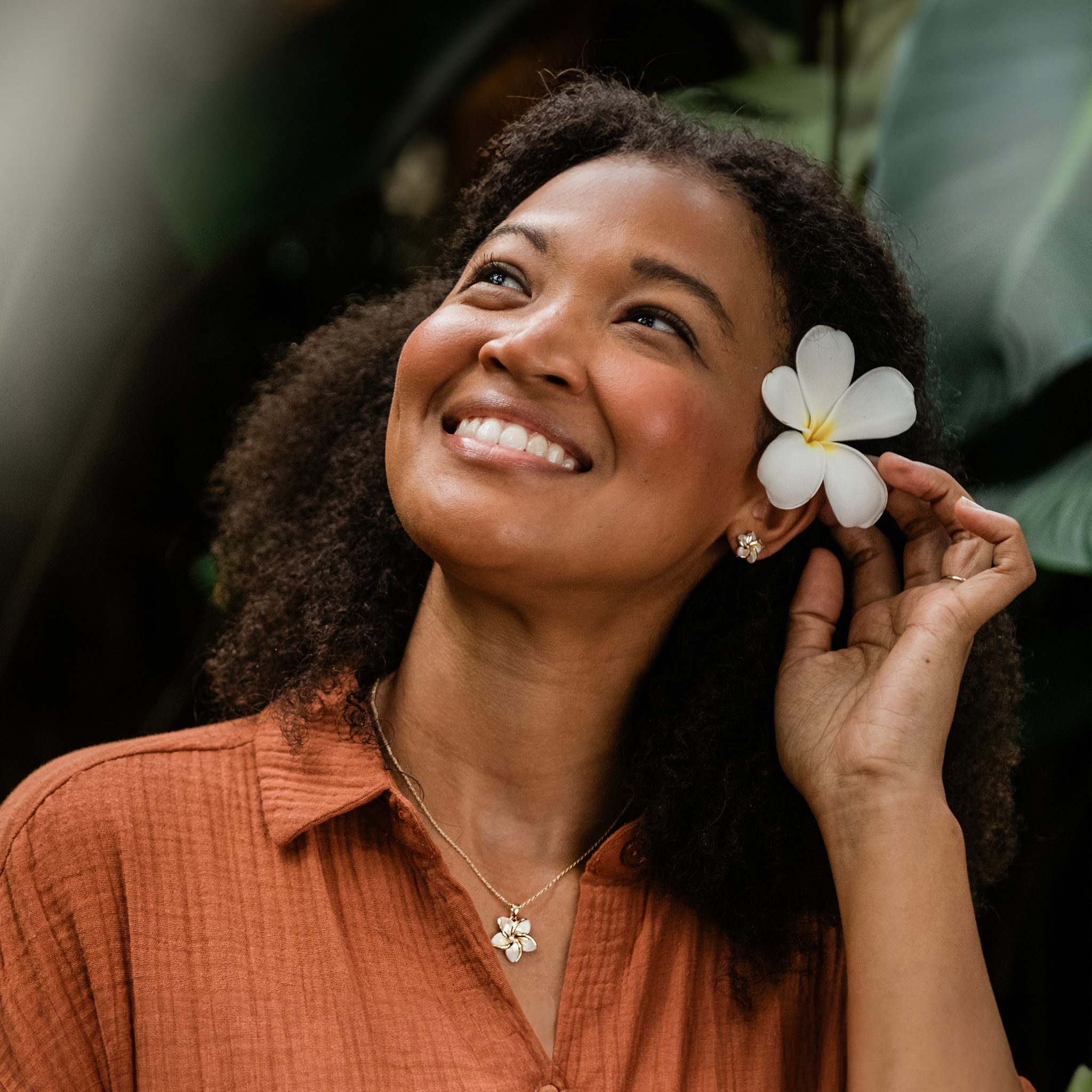 Woman in tropical garden wearing Plumeria Mother of Pearl Earrings and pendant in Gold