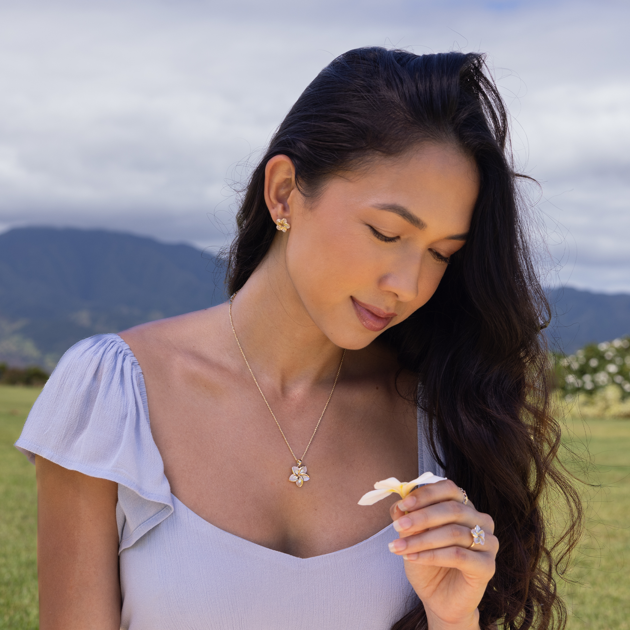Woman sitting on lawn wearing Plumeria Mother of Pearl Earrings, ring, and pendant in 14k Yellow Gold
