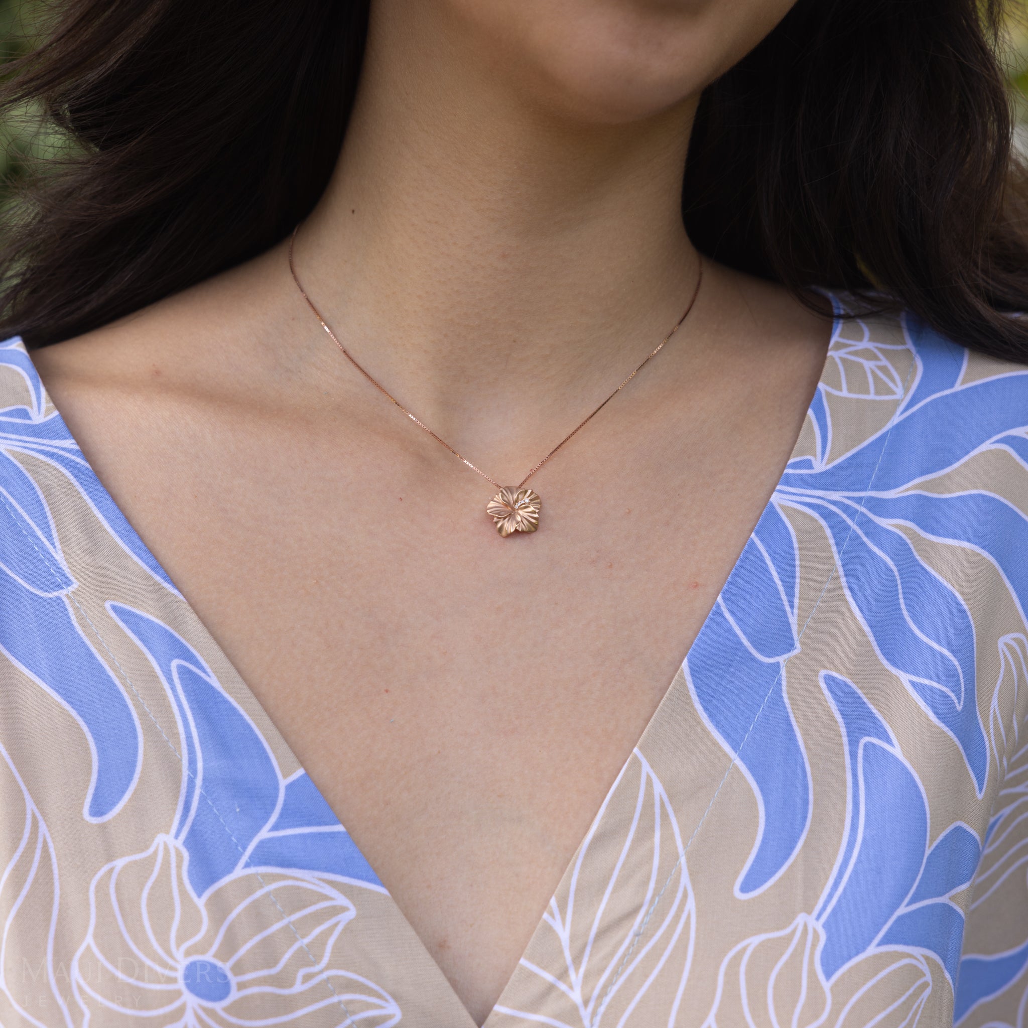 Close up of a person wearing a rose gold diamond hibiscus pendant on a box chain