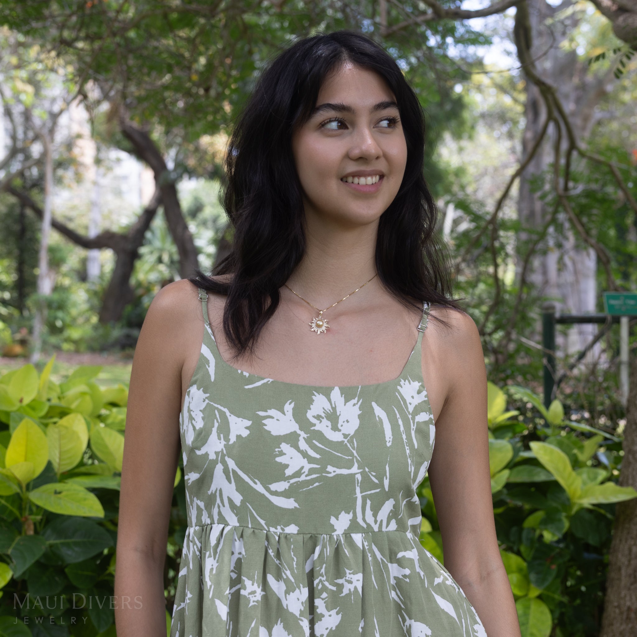 A diamond south sea gold sun pendant in 14k yellow gold worn by a woman in a green patterned dress.
