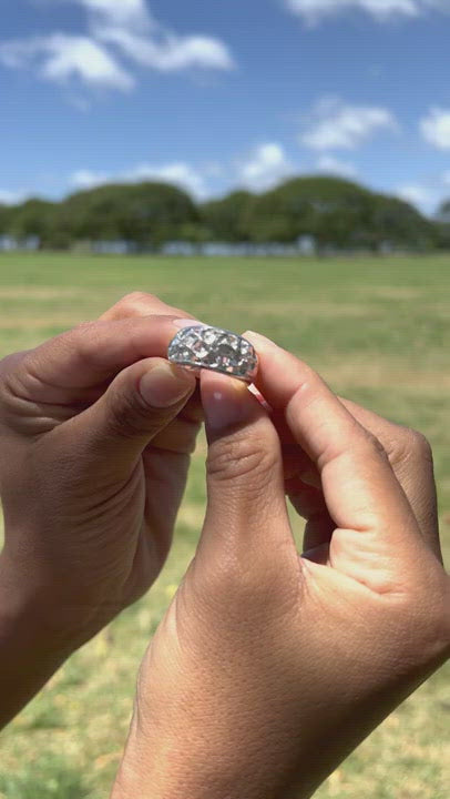 Video of a woman's hand holding a Hawaiian Heirloom Plumeria White Sapphire Ring in Sterling Silver by Maui Divers Jewelry in a grassy field.	