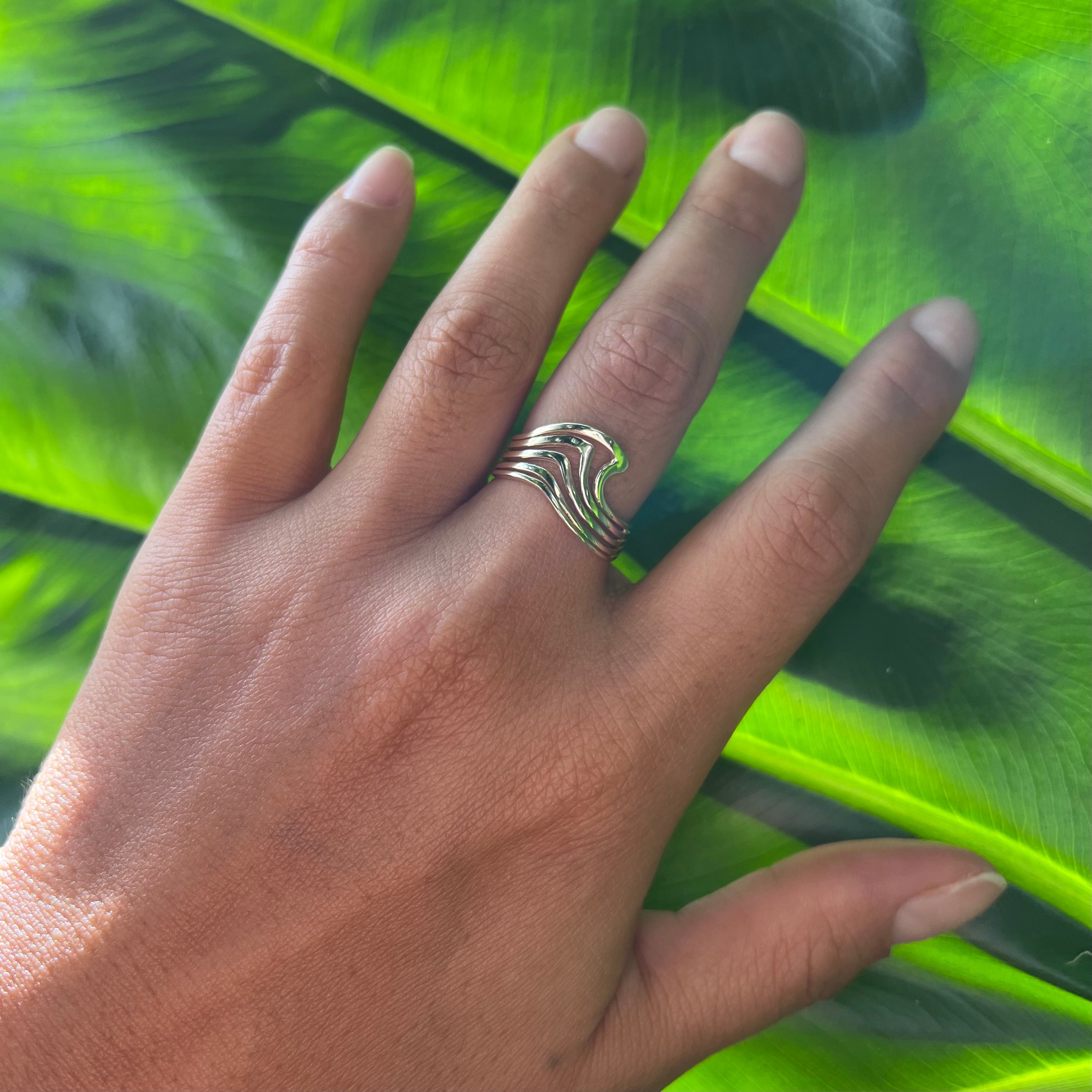 A woman's hand wearing a Nalu Ring in Gold on a leaf background- 11mm - Maui Divers Jewelry