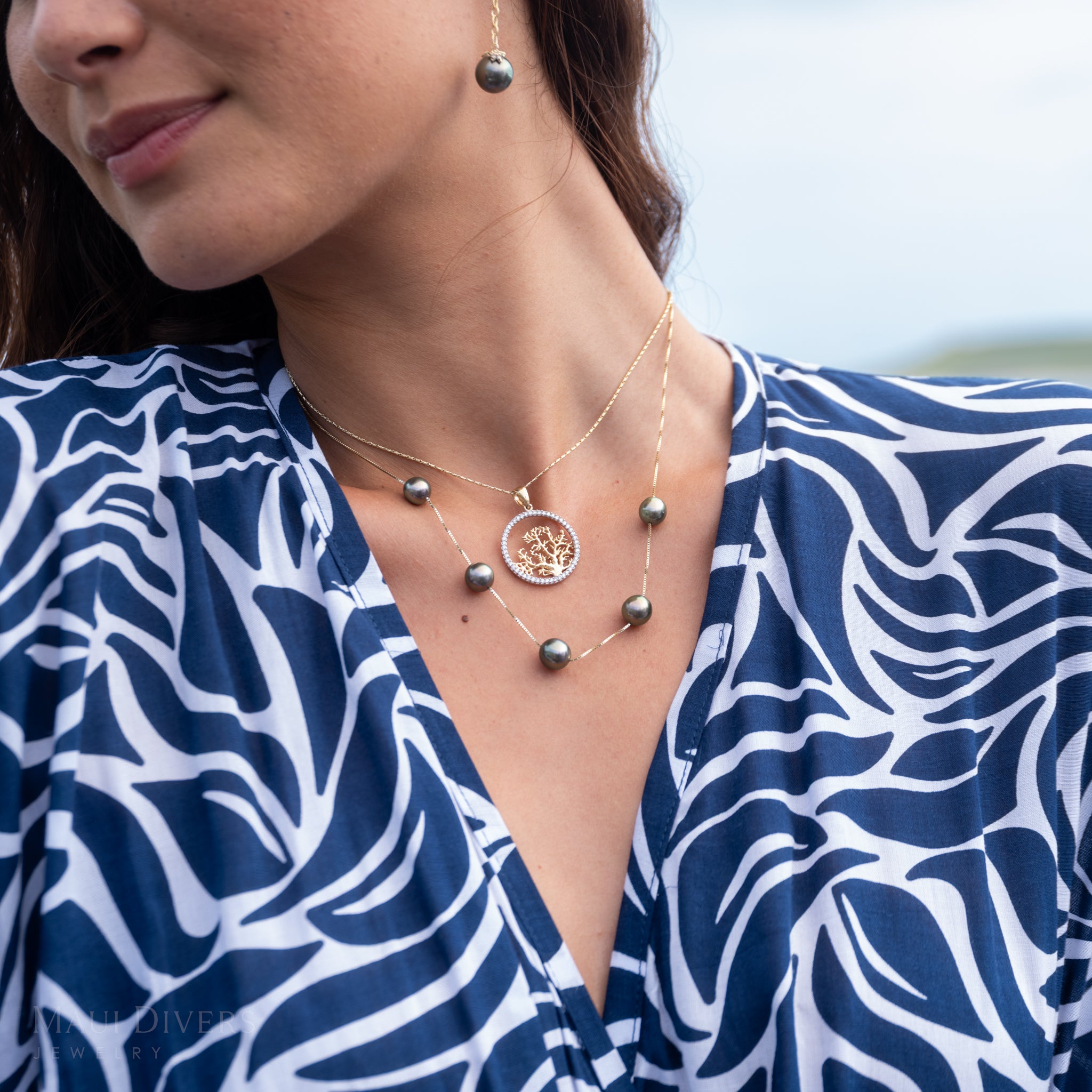 Woman wearing a blue and white patterned top with a five pearl Tahitian black pearl necklace and a diamond coral branch design pendant in white and yellow gold