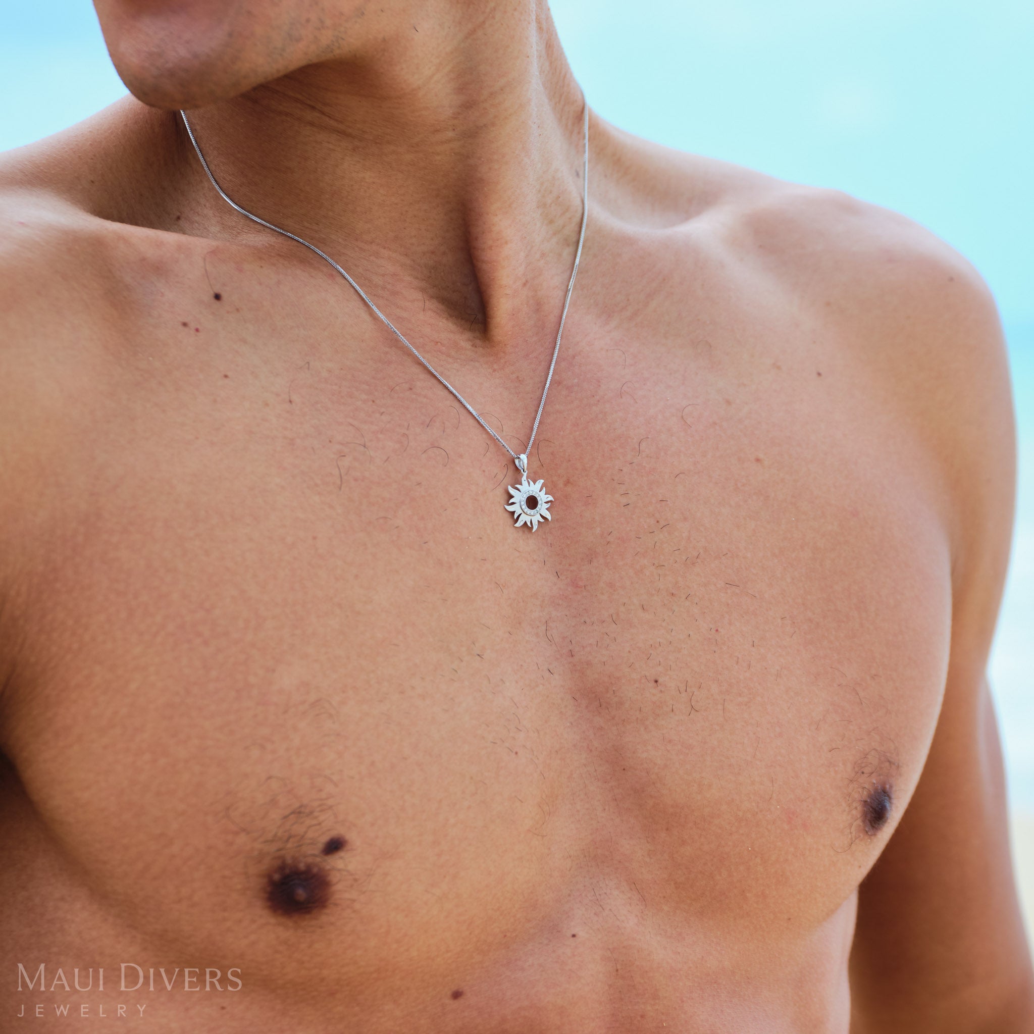 Man wearing a white gold necklace with a sun pendant against a light blue background