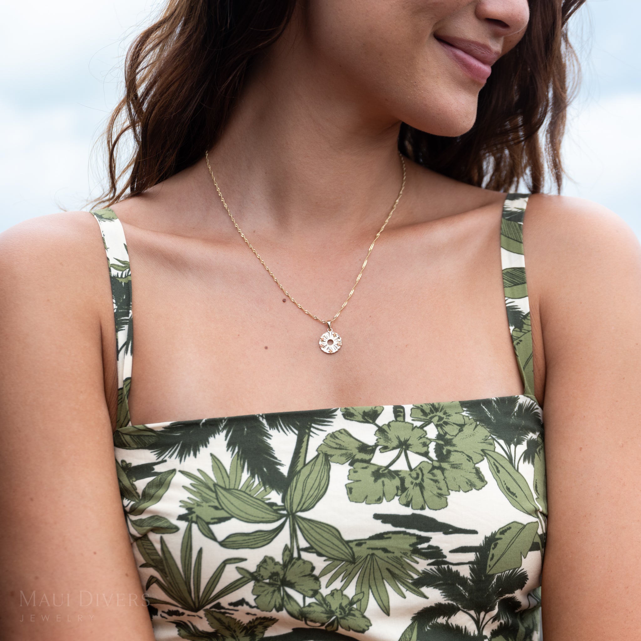 Close-up of a woman wearing a round, gold and orange sapphire pineapple pendant on a singapore chain and a patterned blue and green dress