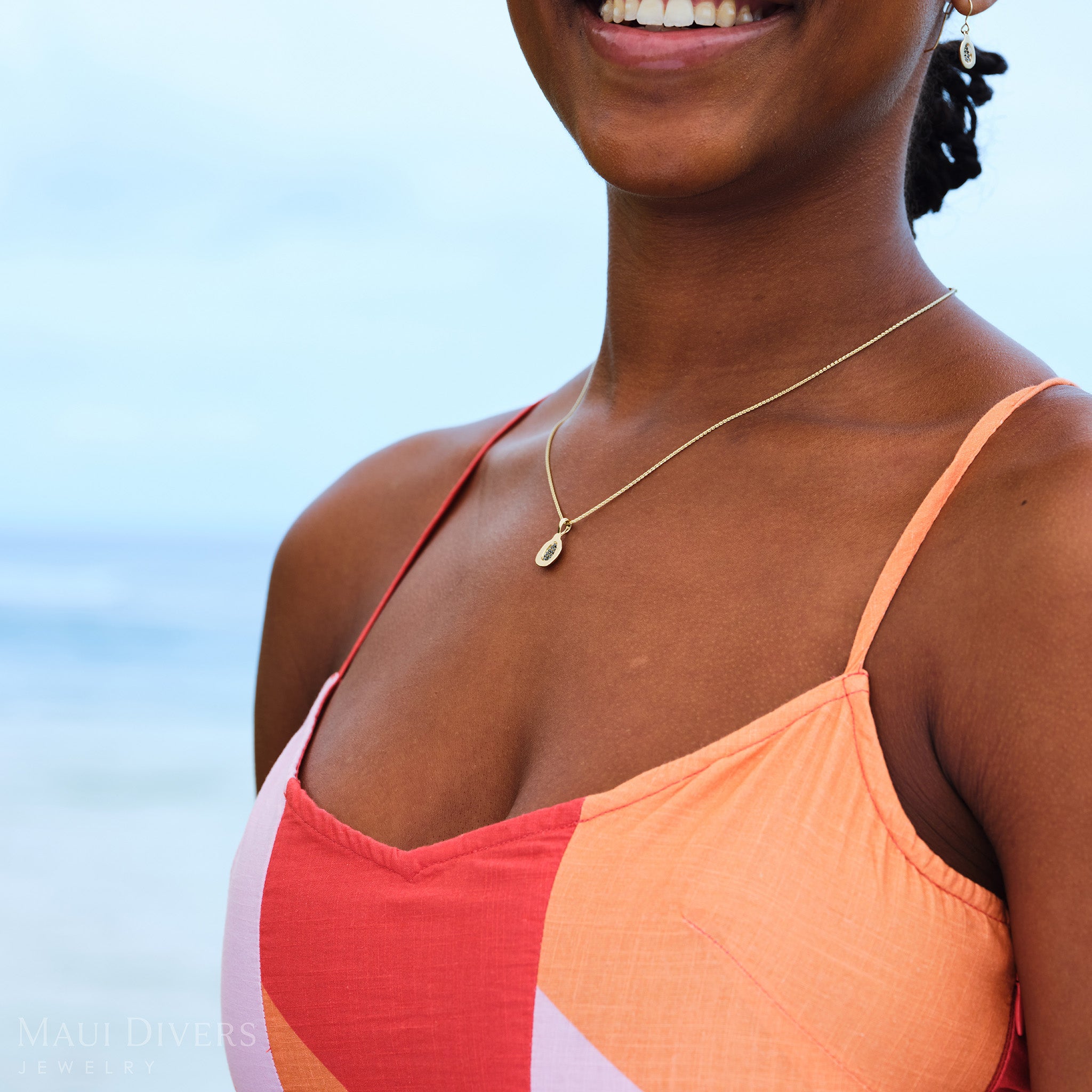 Close-up of a smiling woman in an orange and pink top wearing a Cute Fruits Papaya Pendant in 14k yellow gold with black diamonds around her neck