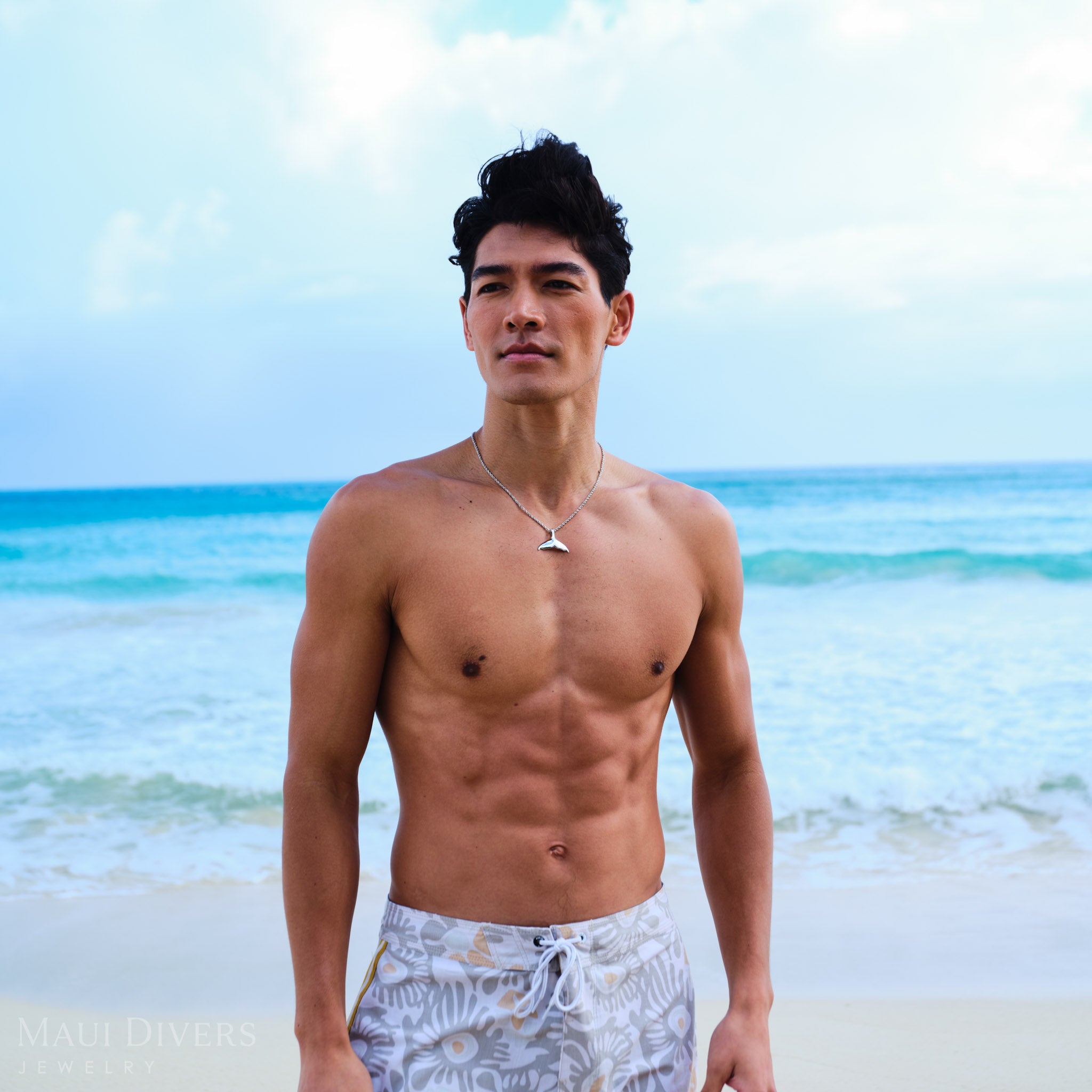 Man wearing a rope chain with a white gold whale tail pendant on a beach